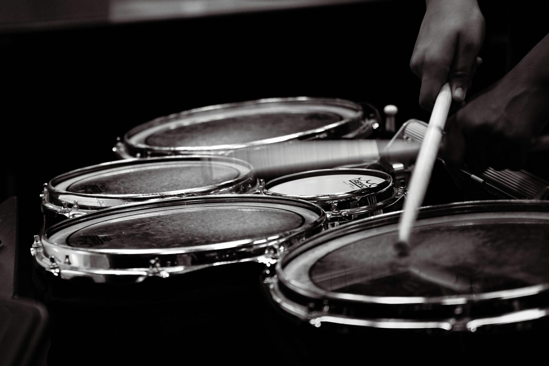 Black and white image of a person playing a set of drums with drumsticks.