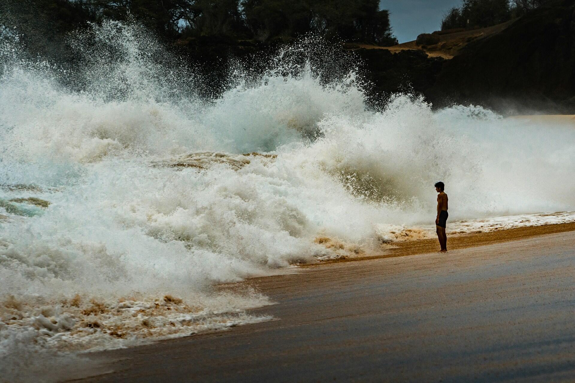 A large wave cresting on a beach directly in front of a person standing there. 