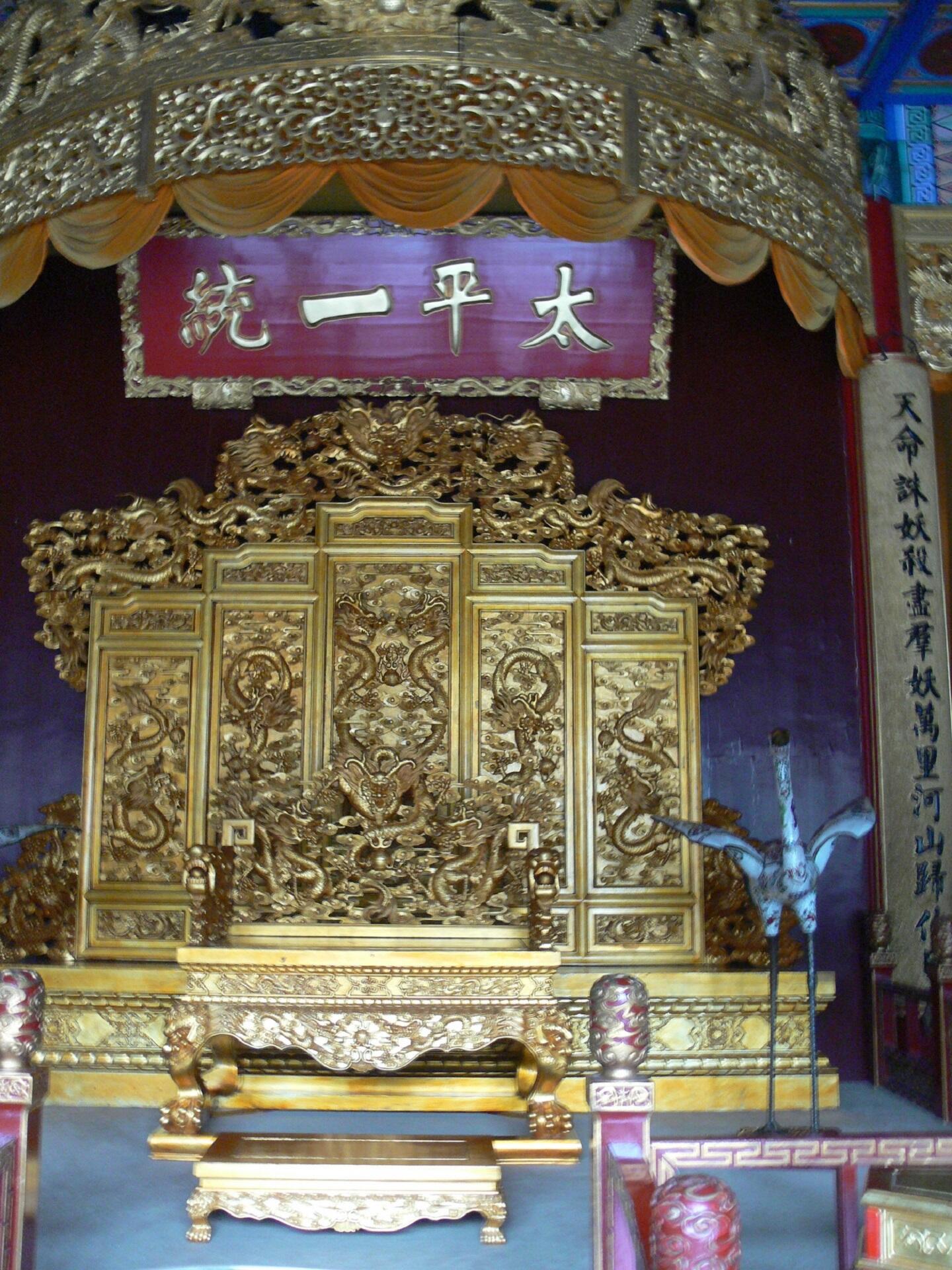 An elaborate golden throne under a red sign with Chinese characters on it.
