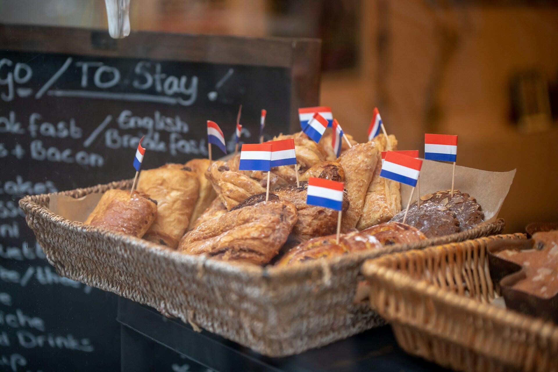A wicker basket filled with various pastries, adorned with small Dutch flags, against a chalkboard menu backdrop.