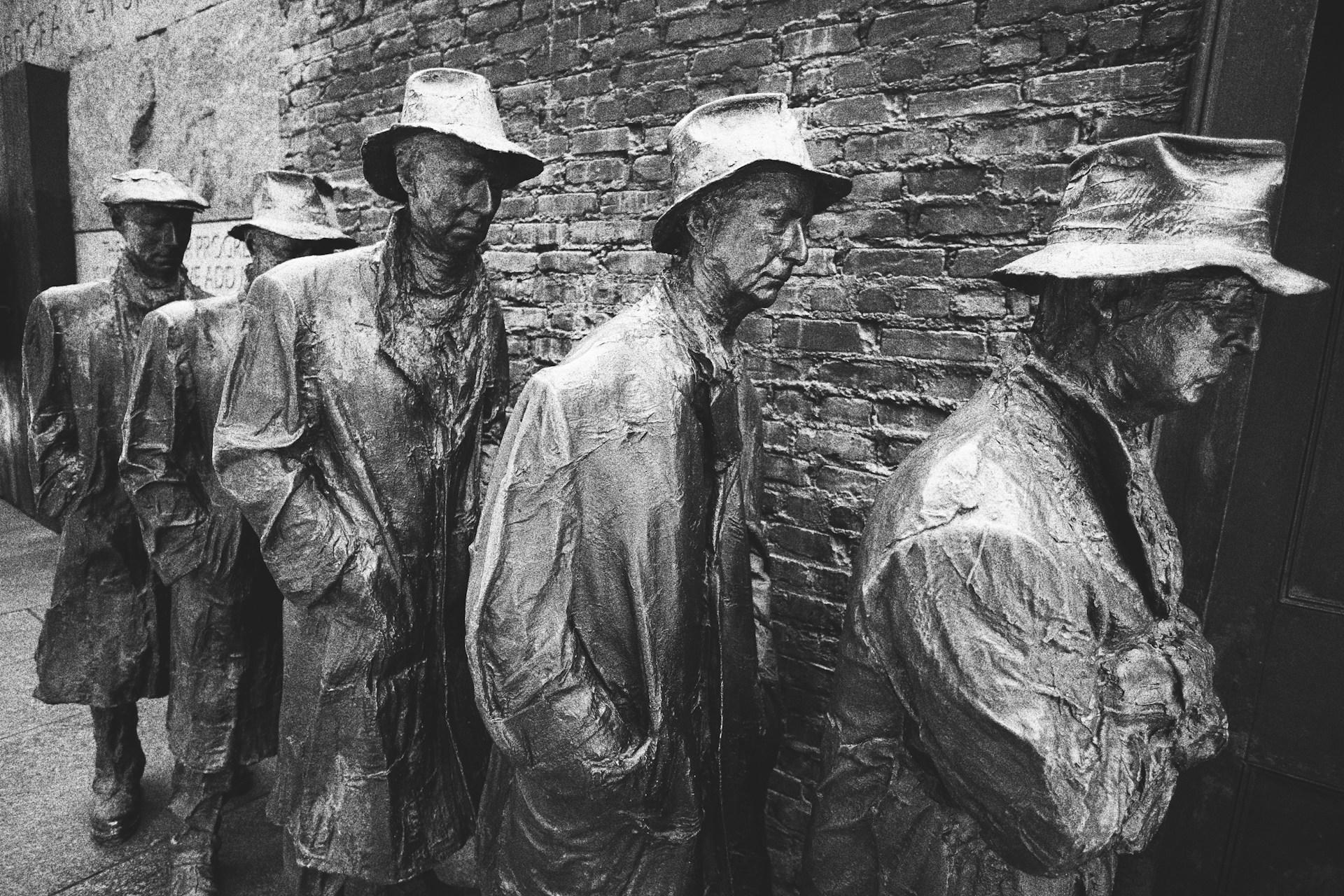 Concrete statues near wall depicting several men in hats and coats waiting in a line