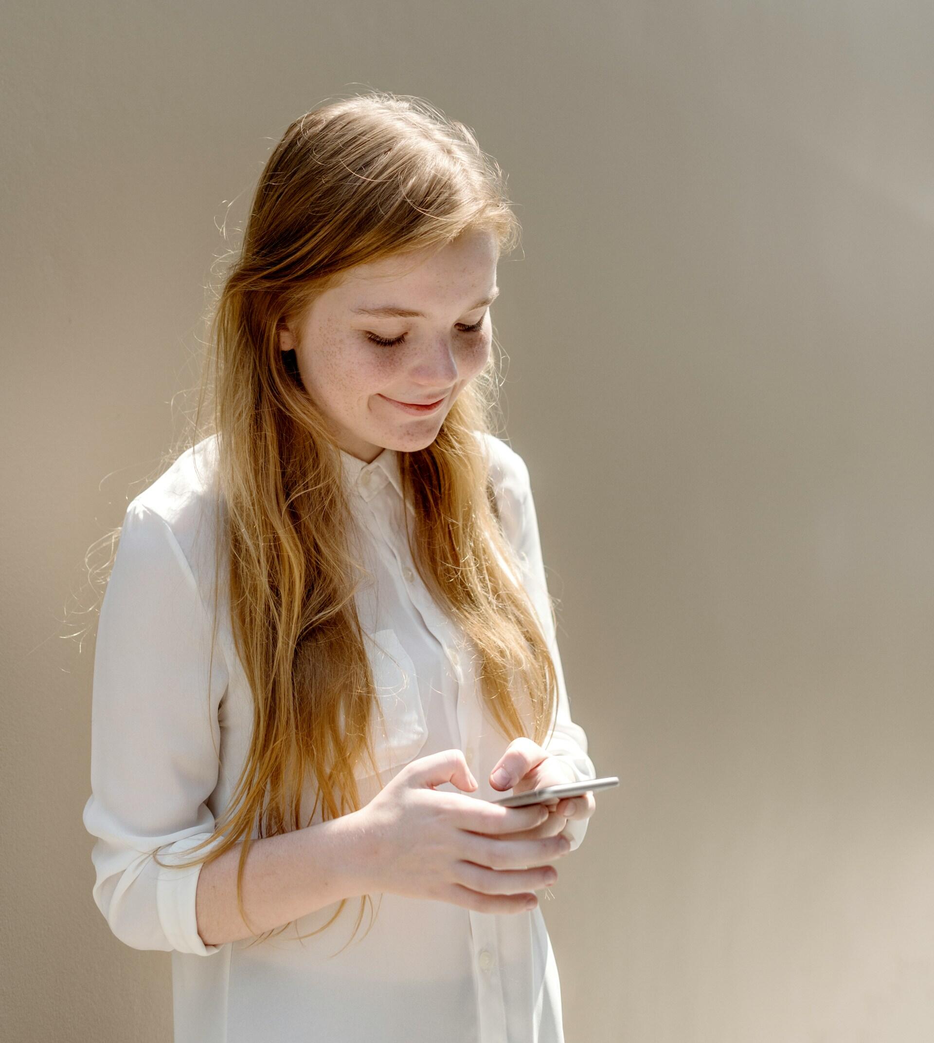 A person with red hair wearing a white shirt uses a smartphone. 