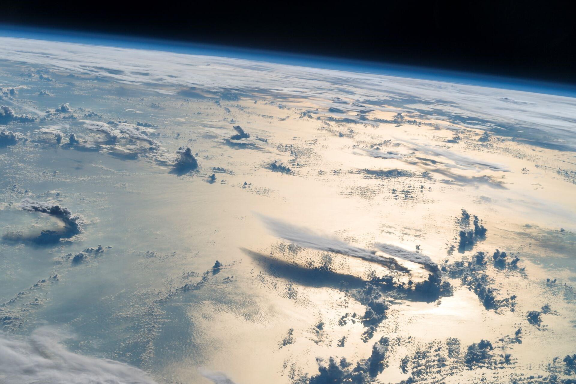 Curved view of Earth from space showing cloud formations over the ocean and atmosphere fading into the darkness of space.
