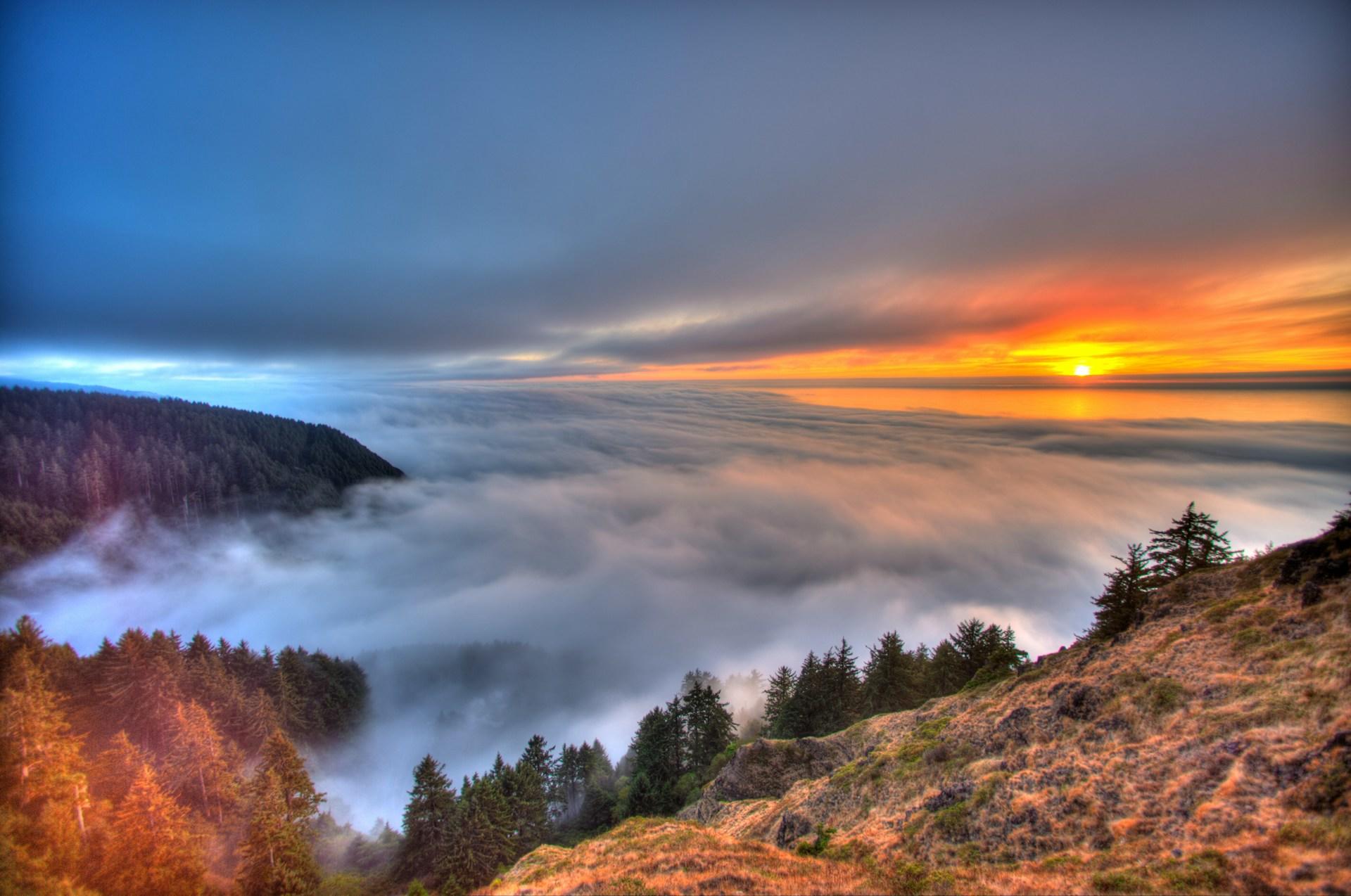 Sunset seen from atop a mountain, with a bluish-grey cloud cover below.