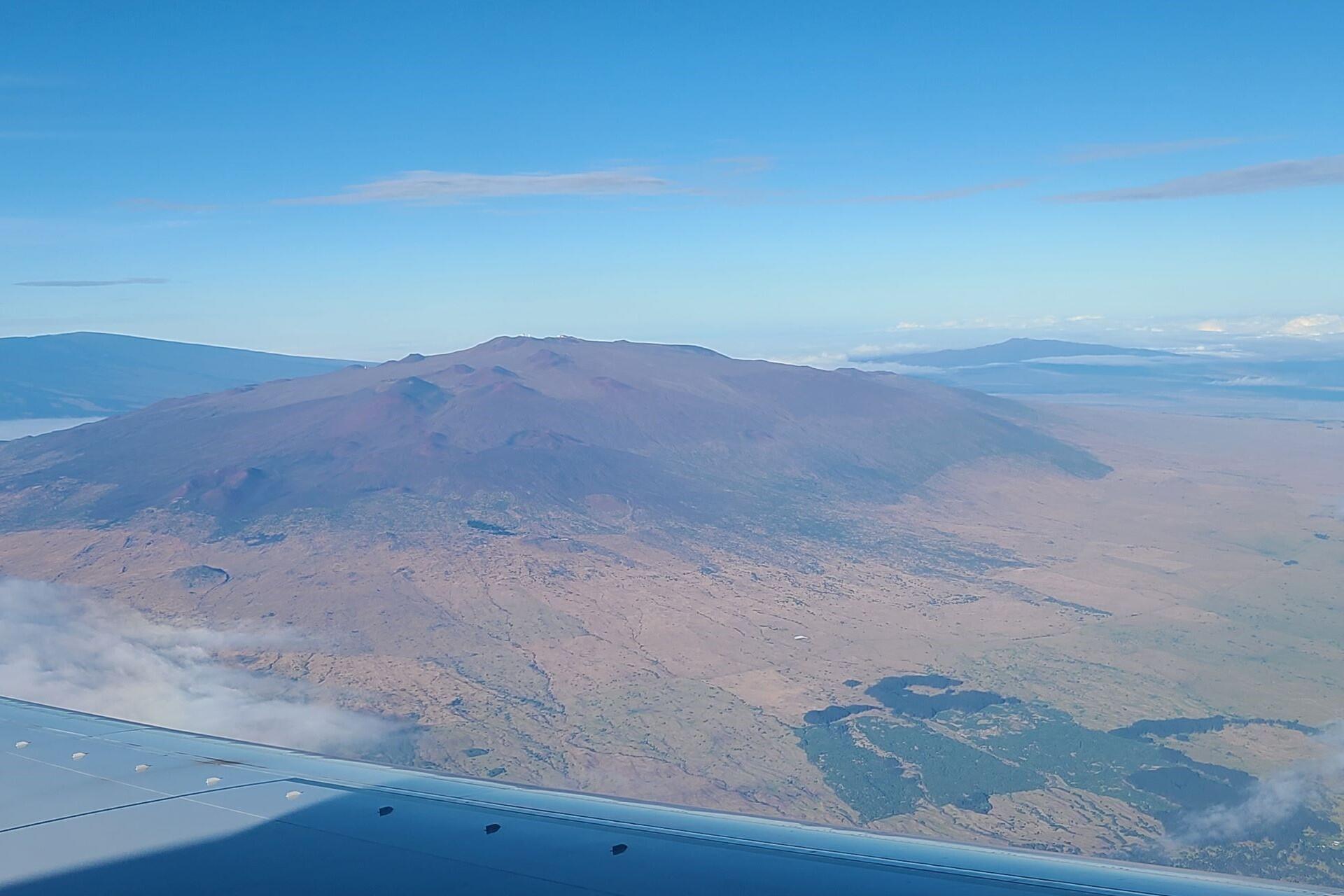 Aerial view of a large volcanic mountain rising above surrounding land with ocean visible in the distance.