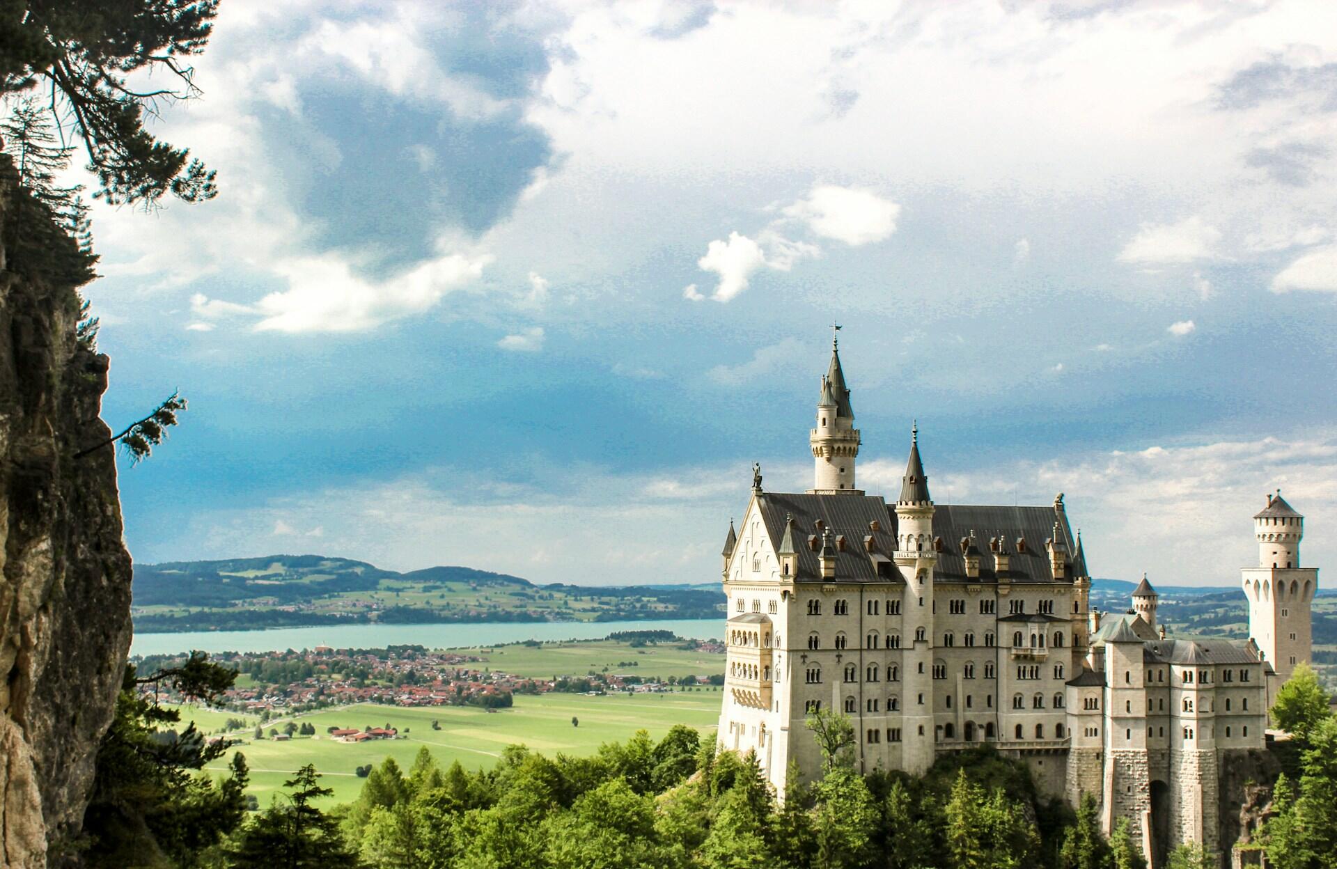 A picturesque view of Neuschwanstein Castle set against a backdrop of lush green hills and a cloudy sky.