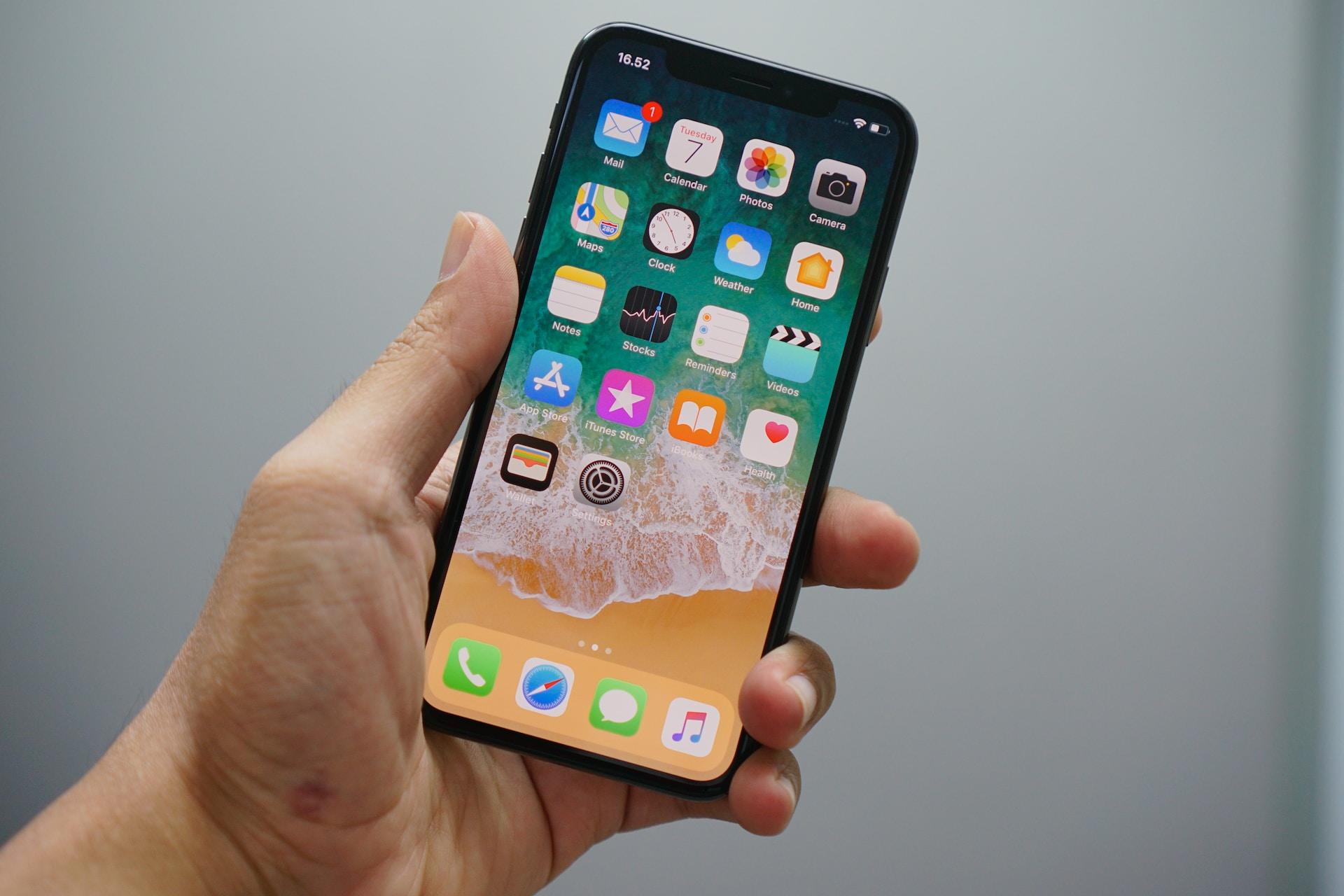 A hand holding an iphone with the apps on the screen.