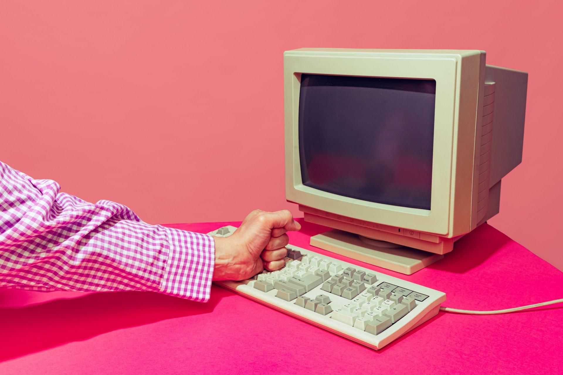 A person's hand on a keyboard positioned beside a computer.