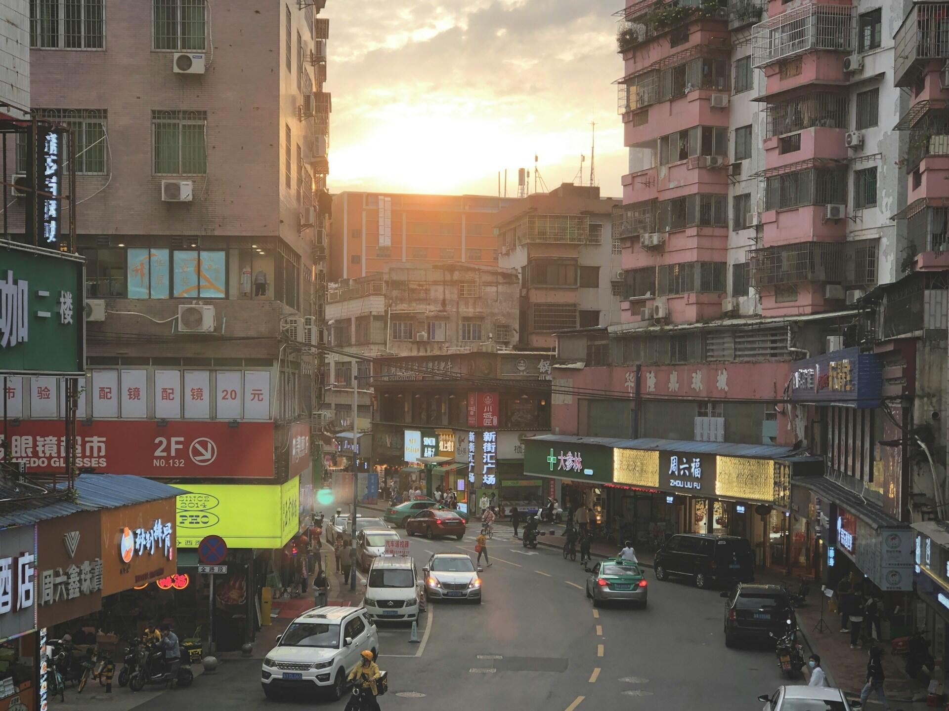 A city street with tall buildings on both sides and cars on the road at dawn.