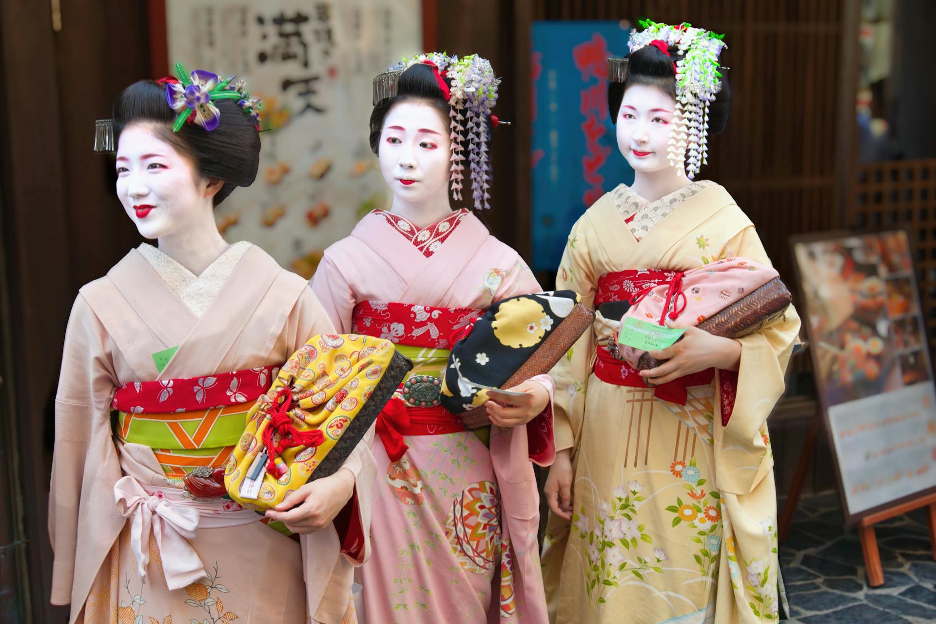 Two maiko and a geisha wearing kimonos with elaborate hairstyles and full makeup