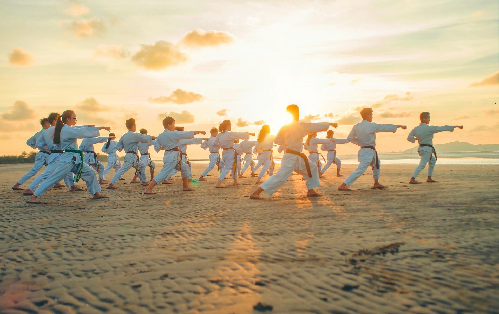 a large group of karate students practicing punches together on a beach