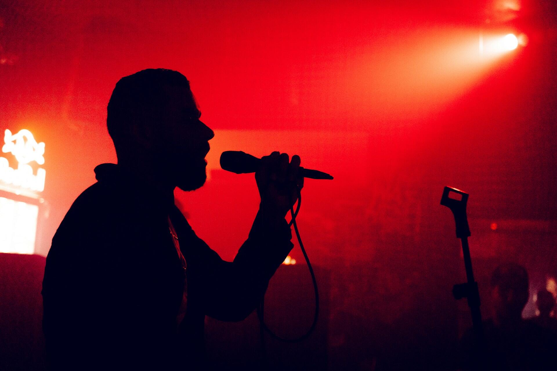 A silhouetted singer holds a microphone on stage.
