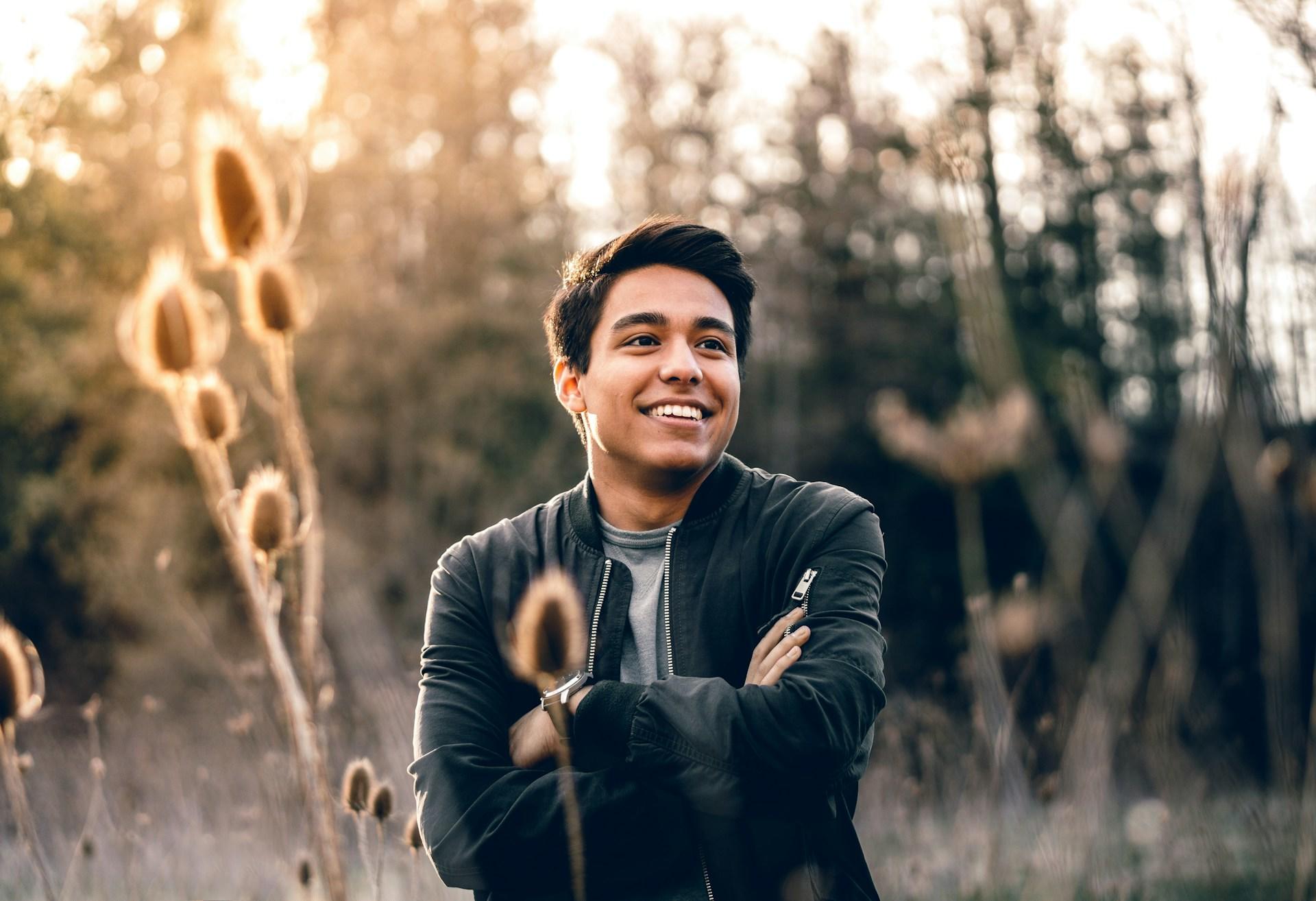 a smiling man standing next to some green trees