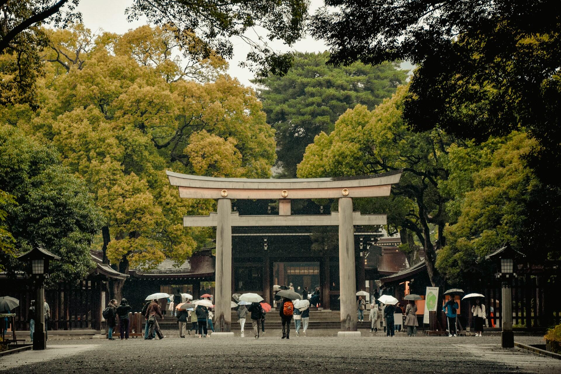 a Shinto torii gate with about a dozen people passing beneath on a rainy day