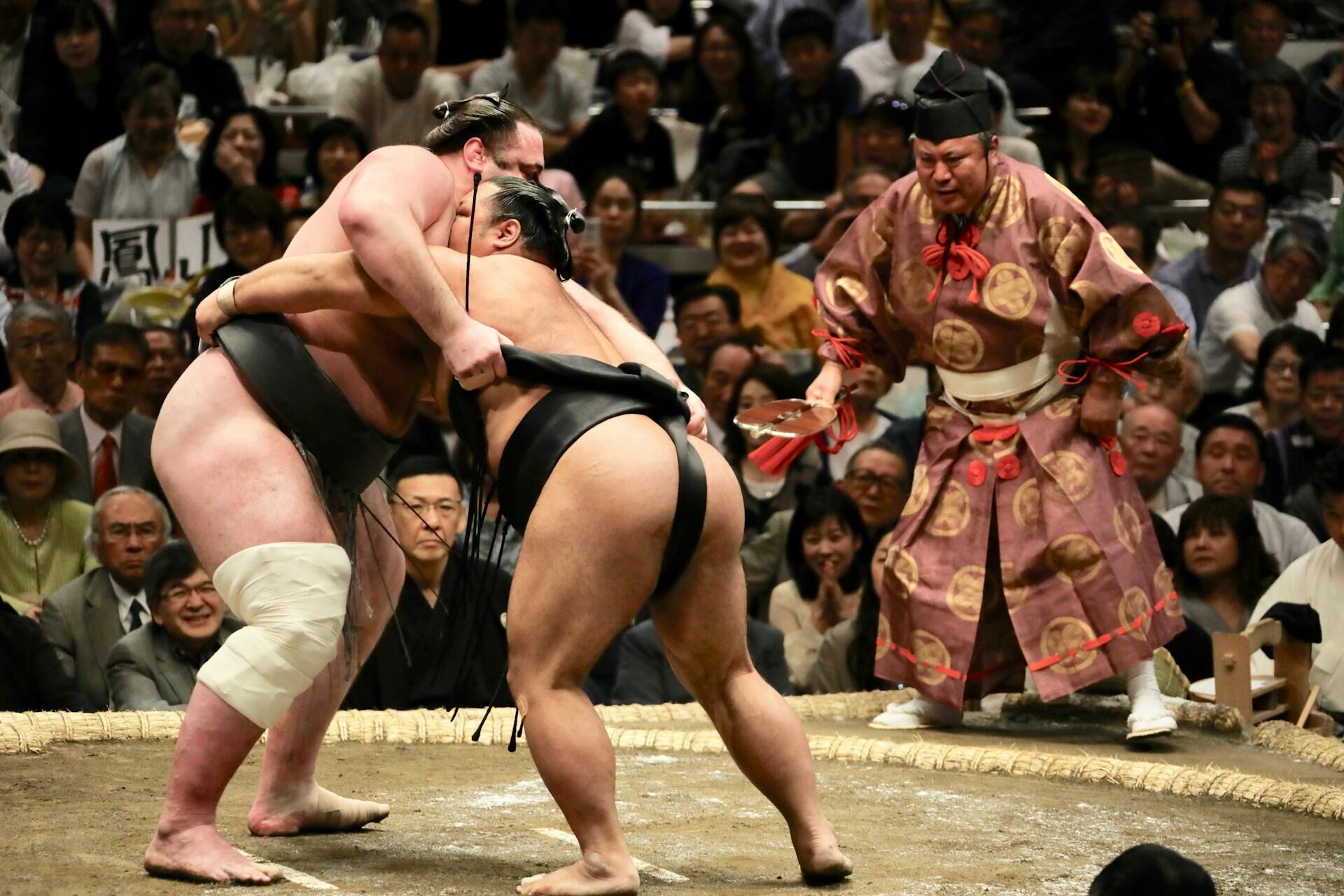 two sumo wrestlers in the ring each grabbing each other's belts