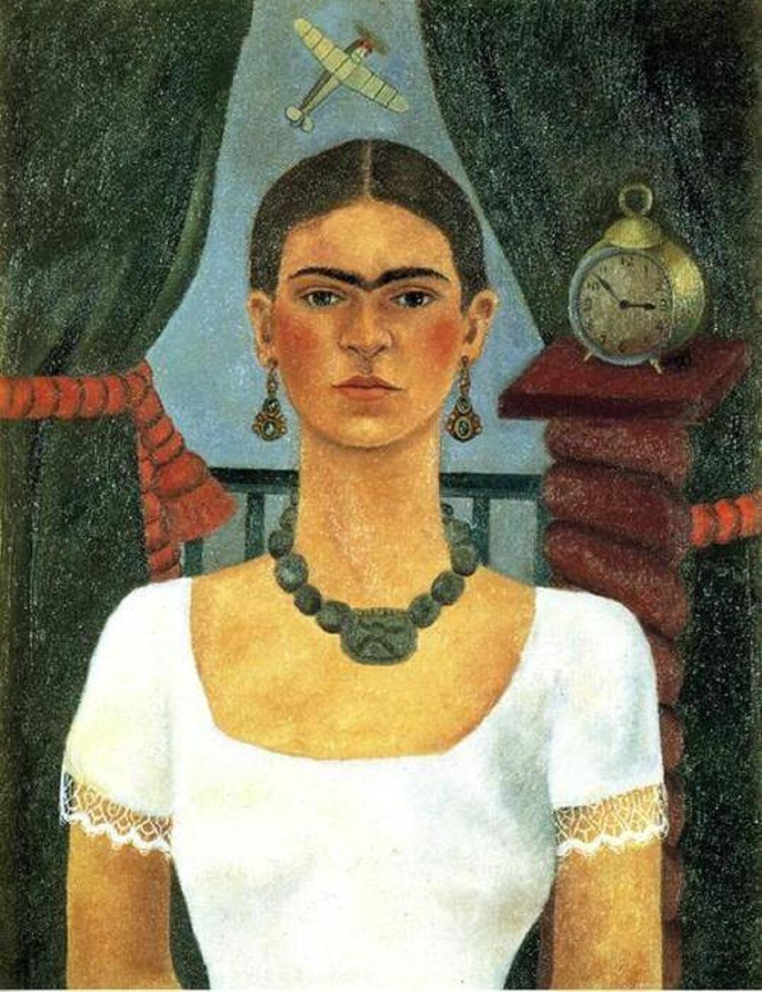 A woman in a white dress with a green necklace in front of a window.