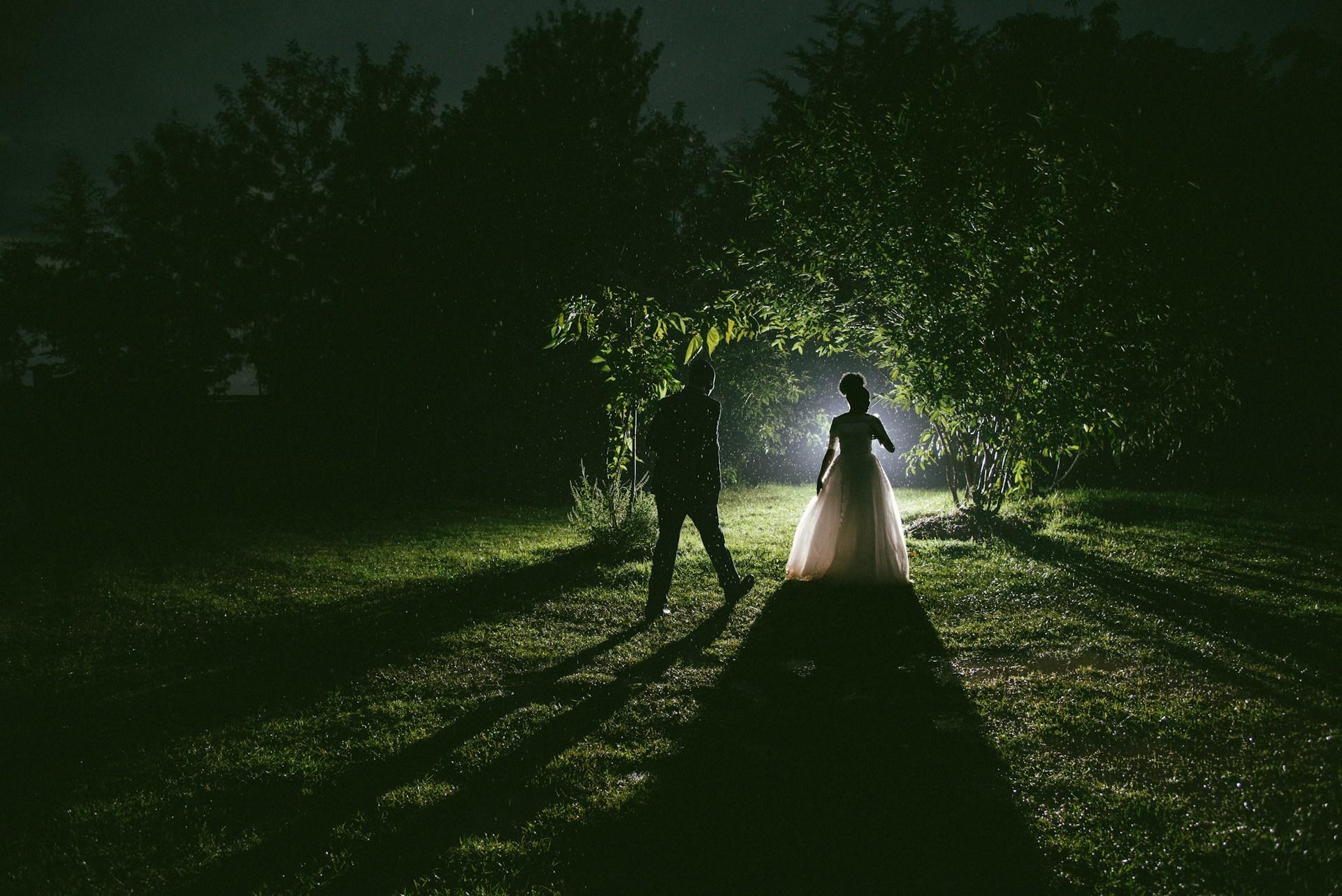 Man and woman walking on pathway between trees during nighttime