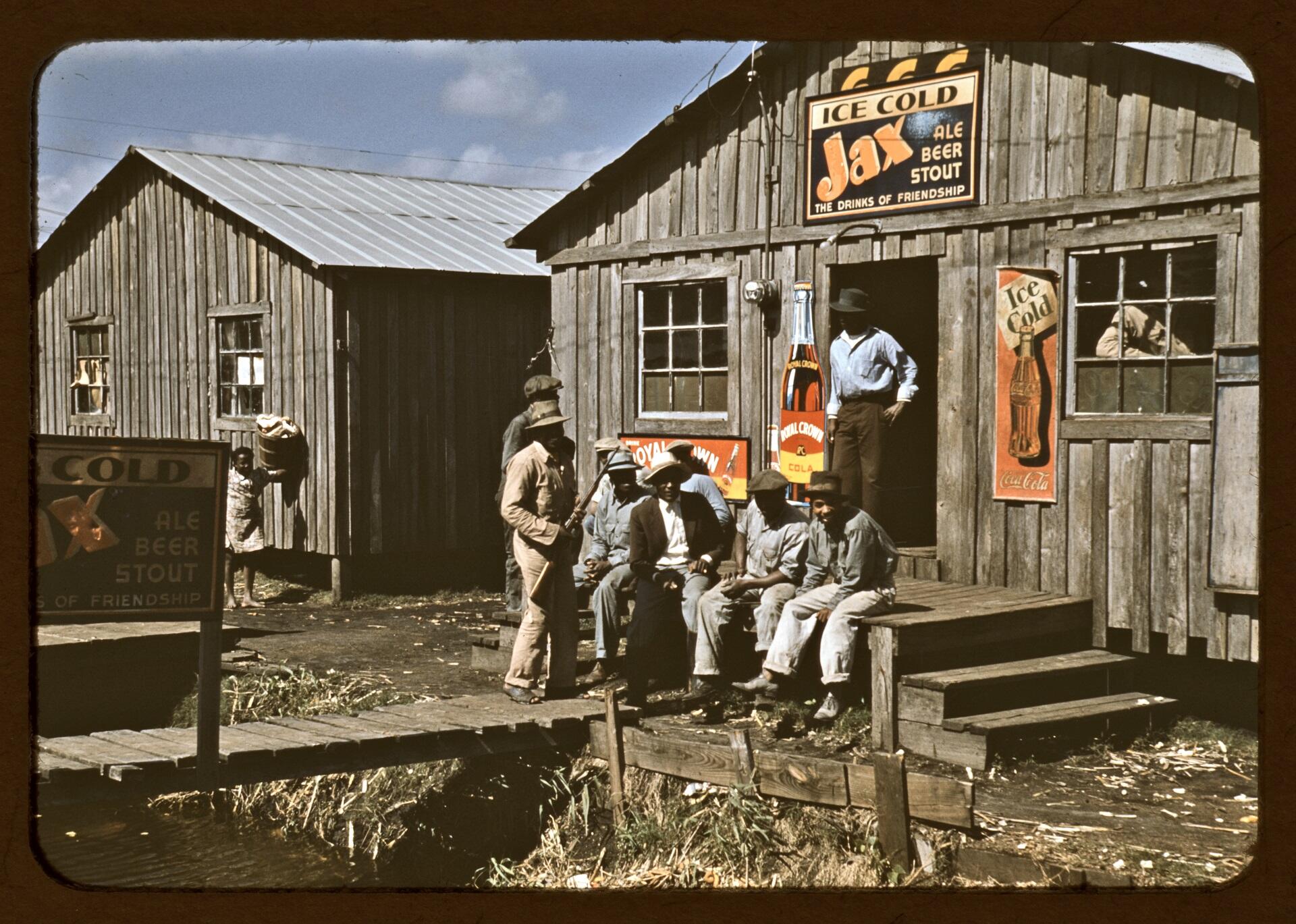 Men and boys gathered in front of a wooden building with adverts on it.