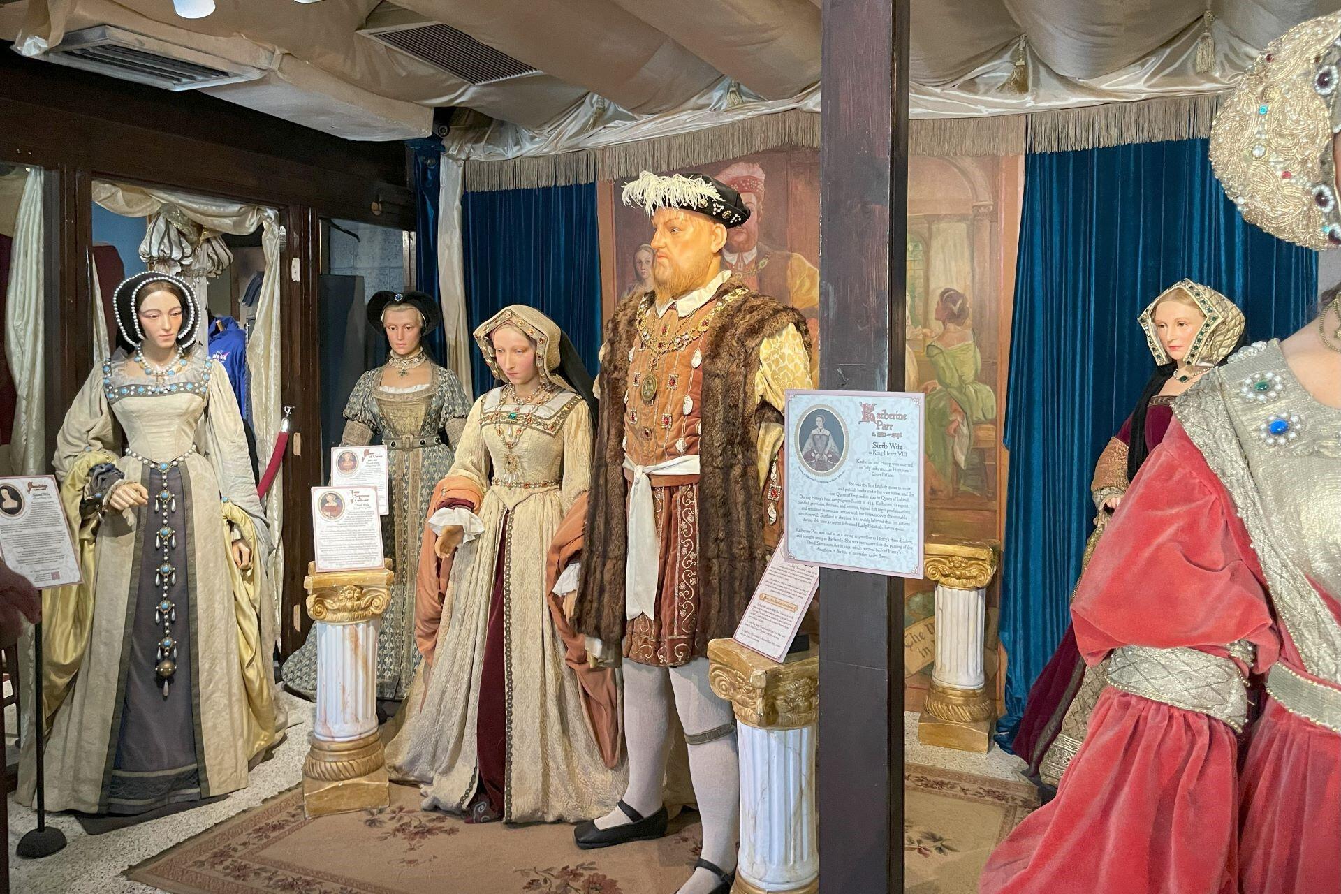 Wax figures of Tudor monarchs and royal figures dressed in period clothing displayed in a museum exhibit.