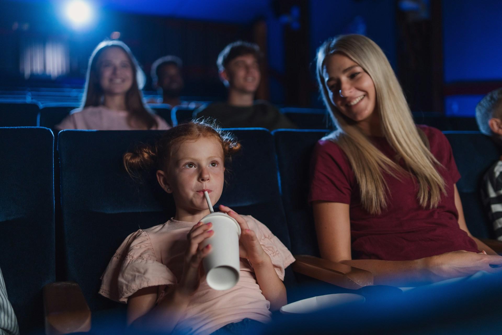 A mother with a small child in the cinema watching film and drinking with a straw.