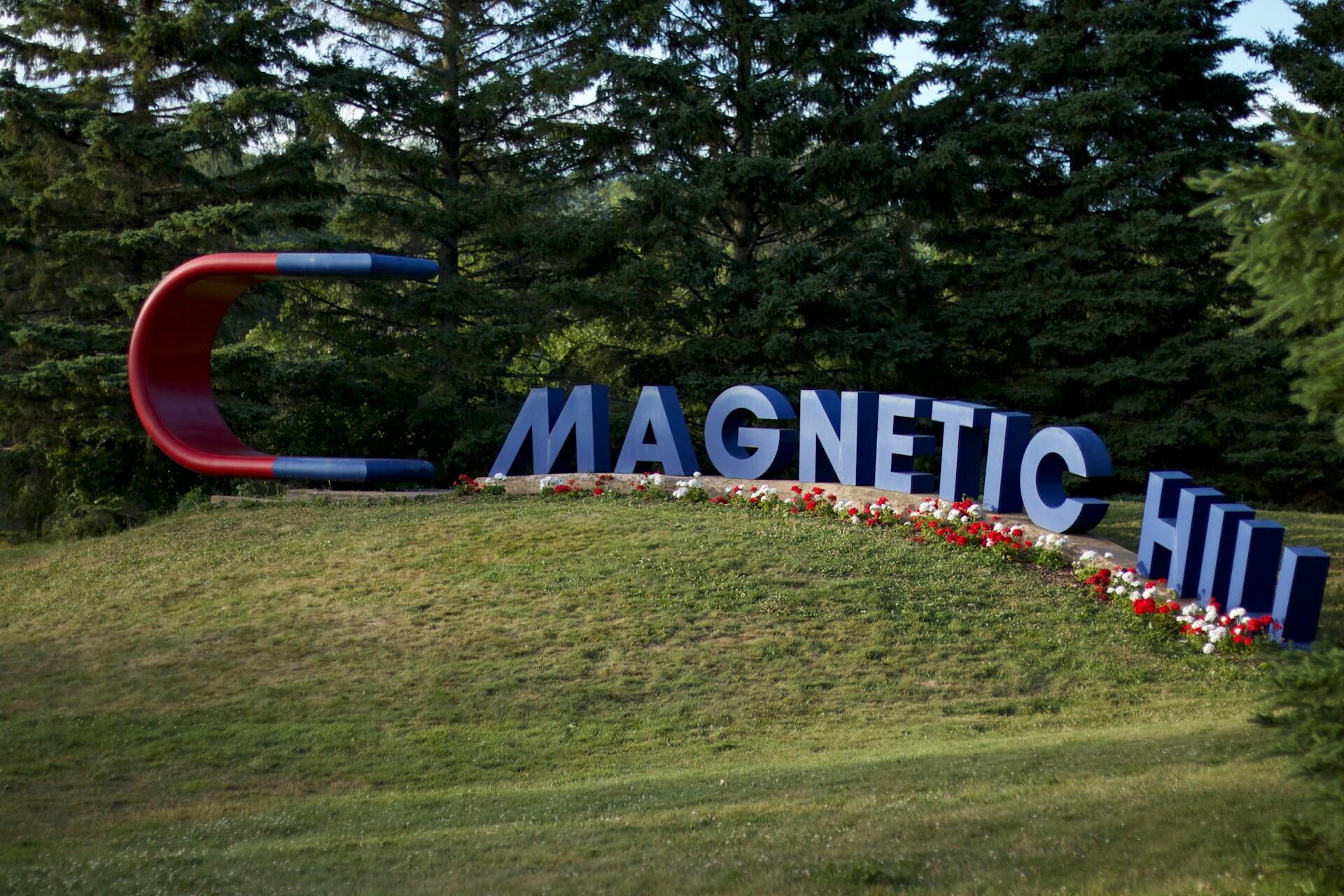 A large red and blue magnet on a small knoll with the words magnetic hill in front of it. 