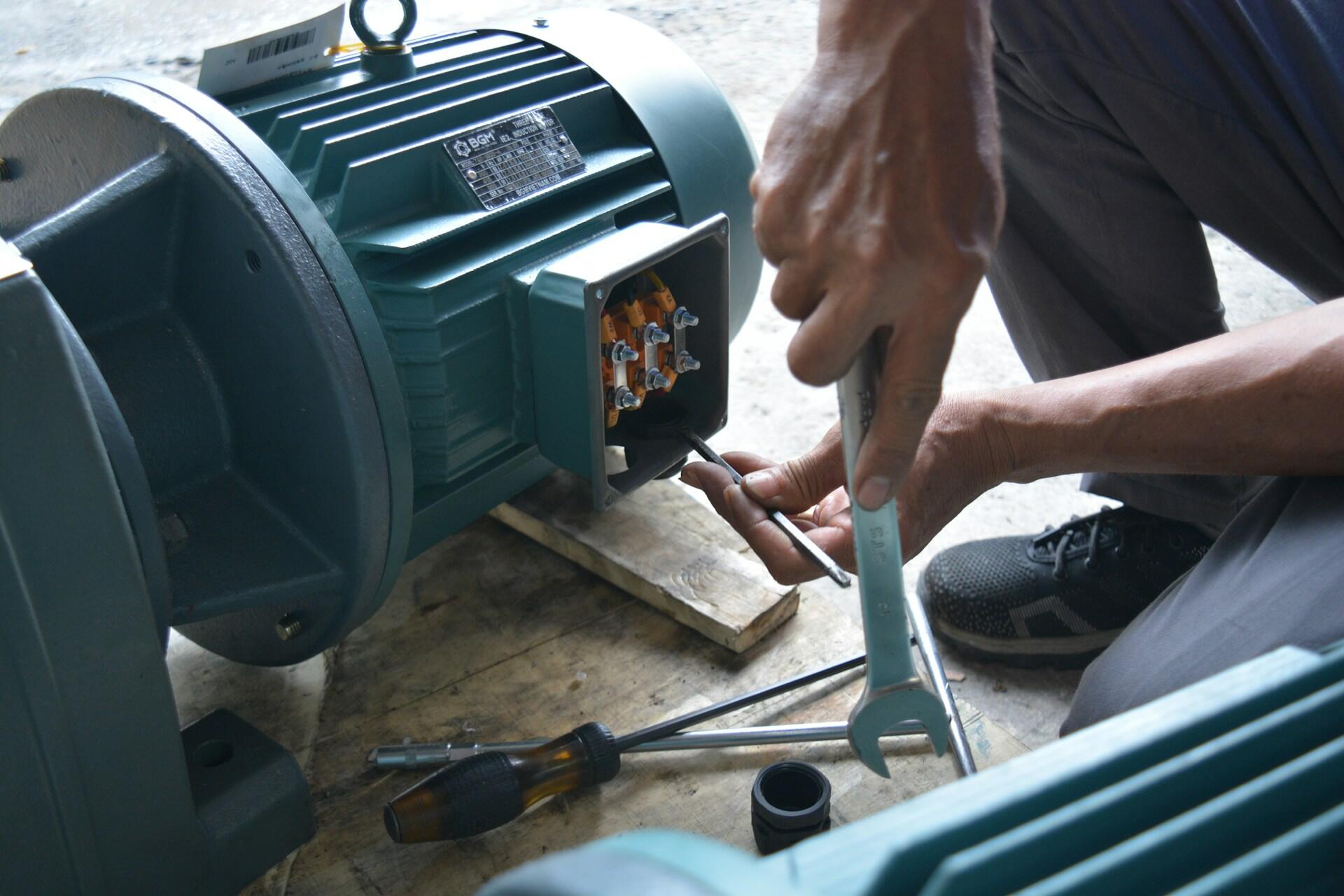 A person with a tool in their hand next to a motor.