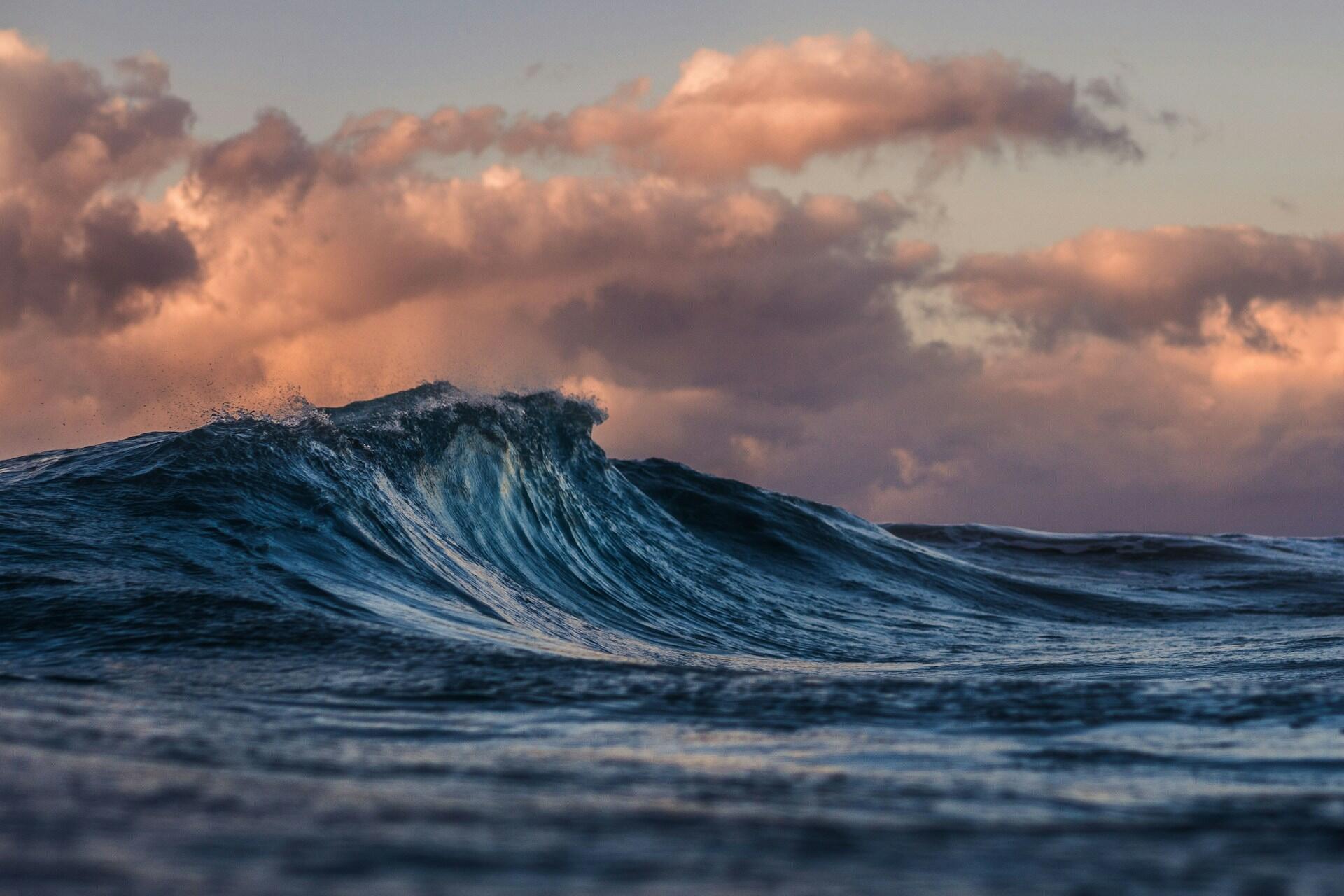 A tall ocean wave under a cloudy sky. 