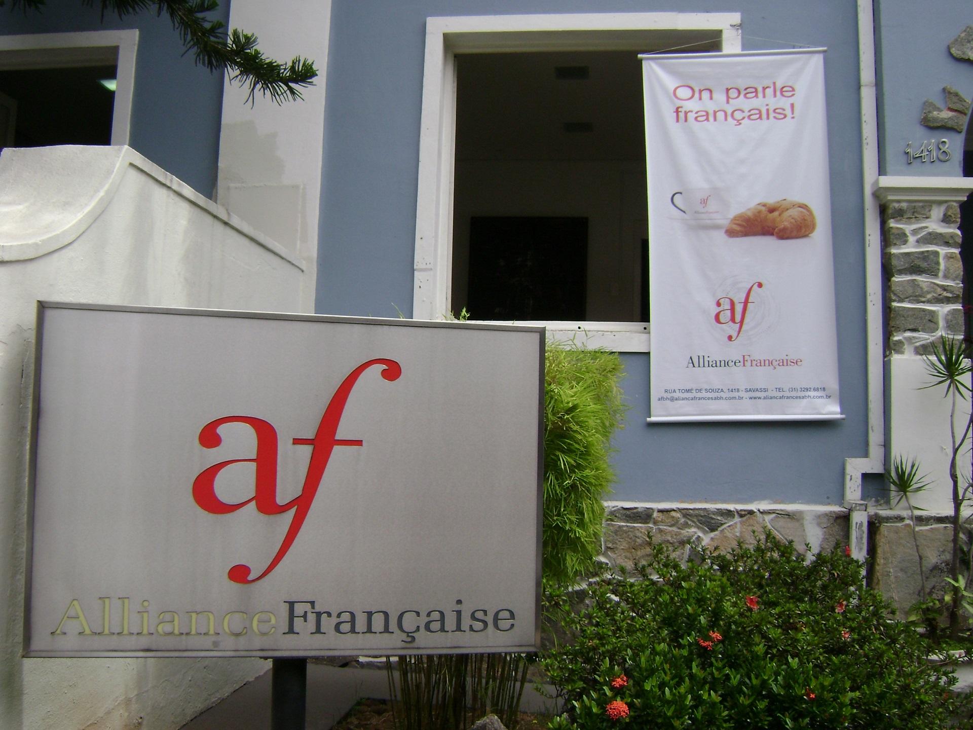 A powder-blue structure bearing a white sign with a croissant and the Alliance française logo in red, with a standalone grey sign bearing the same logo. 