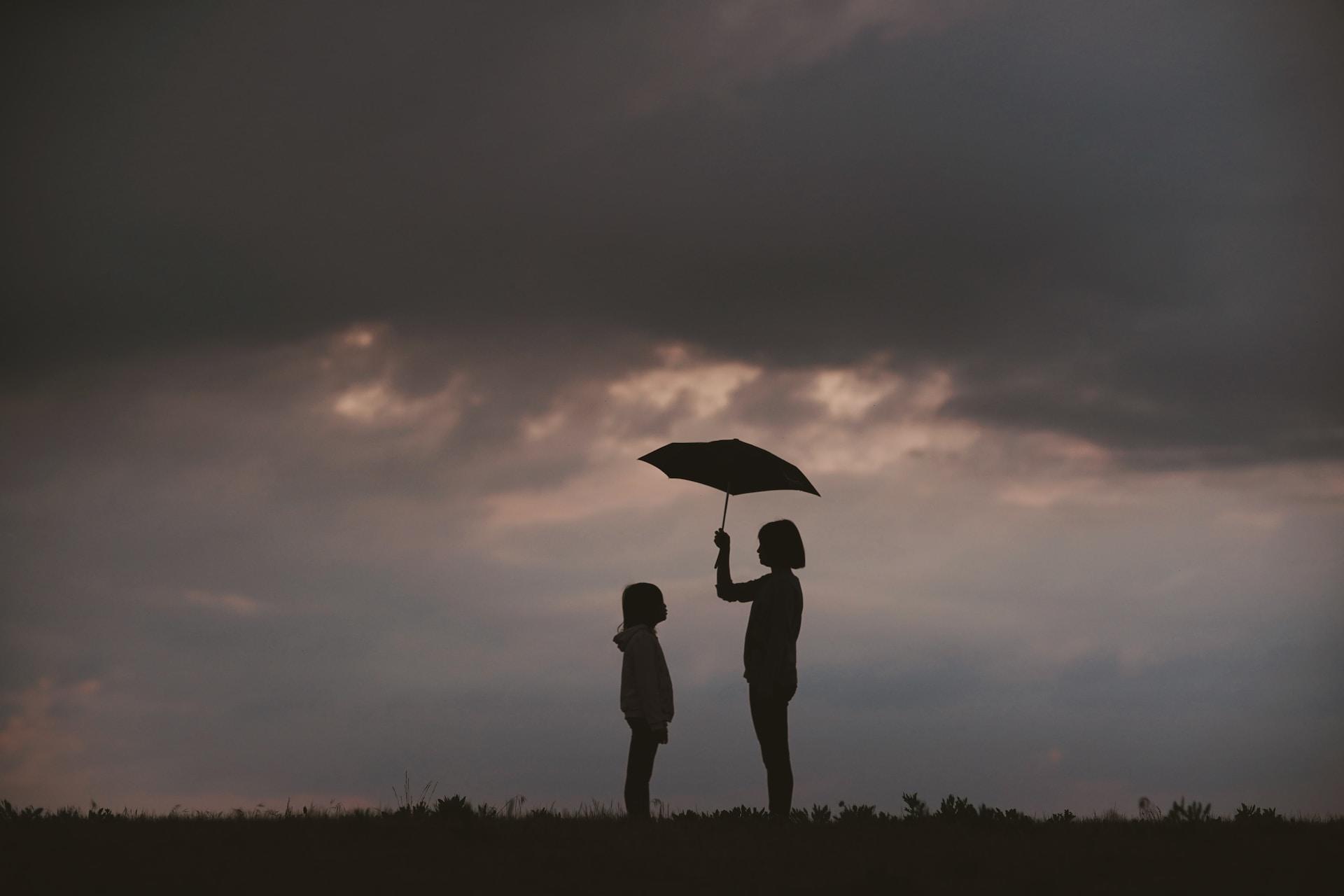 Two people seen in silhouette facing one another under a dark cloud, with the taller person holding an umbrella to shelter the shorter person.