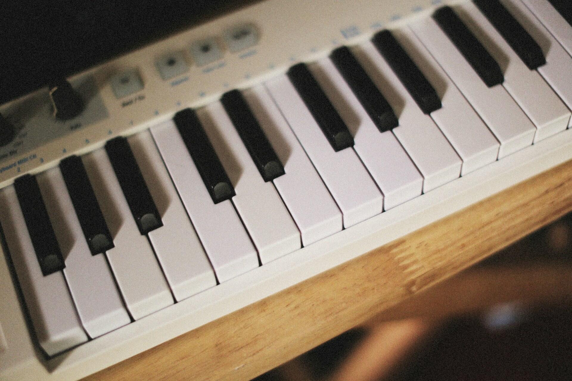 Close-up of piano keys featuring alternating black and white keys on a light-colored keyboard with control knobs above.