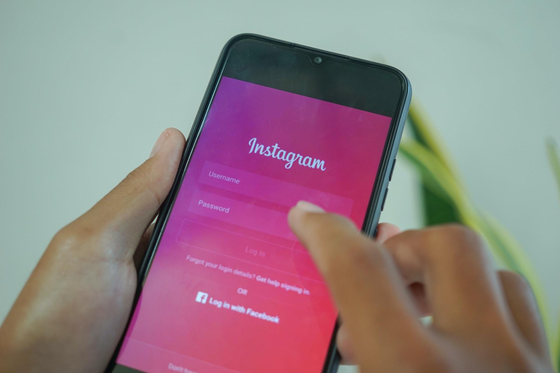 A person holding a mobile phone displaying a hot pink instagram login screen 