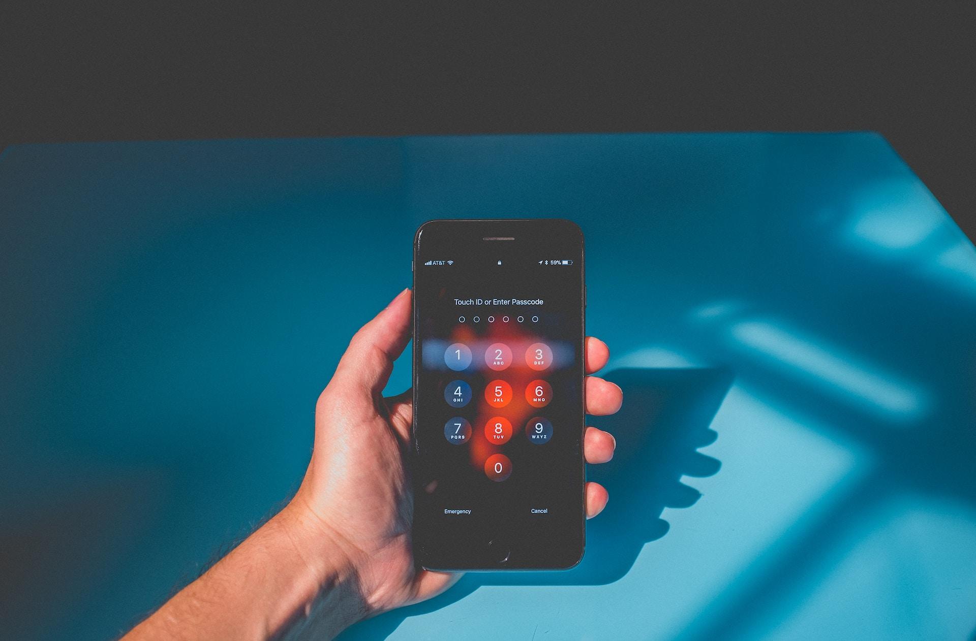 A hand holding a smartphone with its screen in dark mode showing a flame of orange to highlight the keypad, set against a bright blue background.