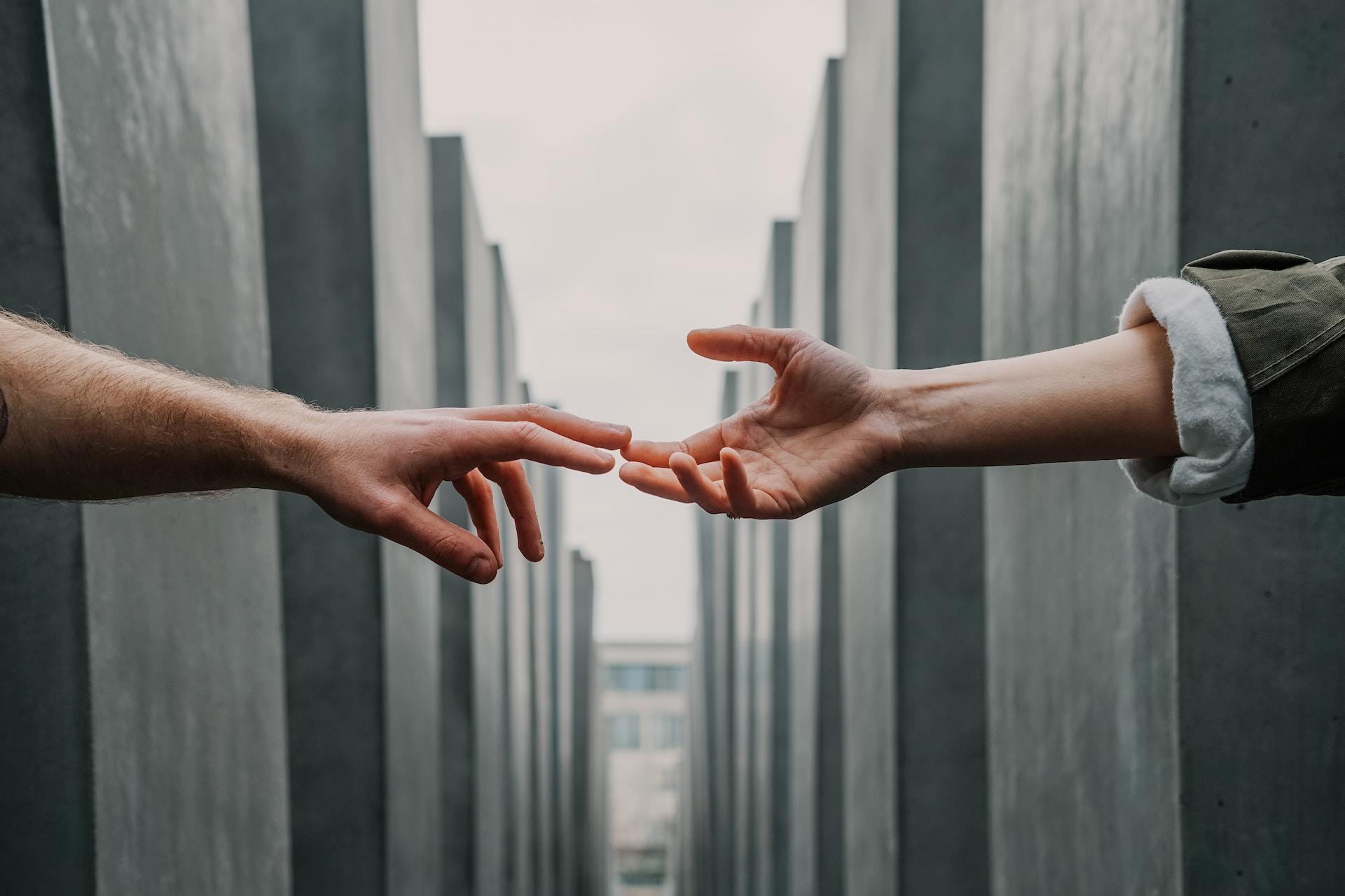 Two hands reaching out to one another across a stark divide marked by grey walls.