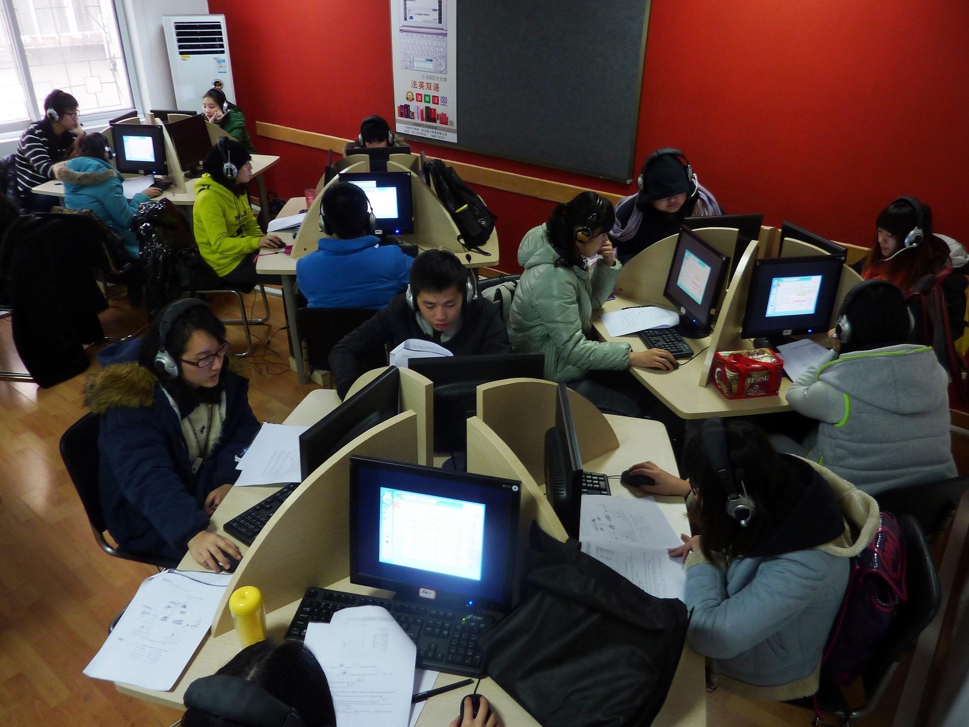 A room with red walls and several round tables segregated into self-study areas featuring computers, with nearly every seat occupied.
