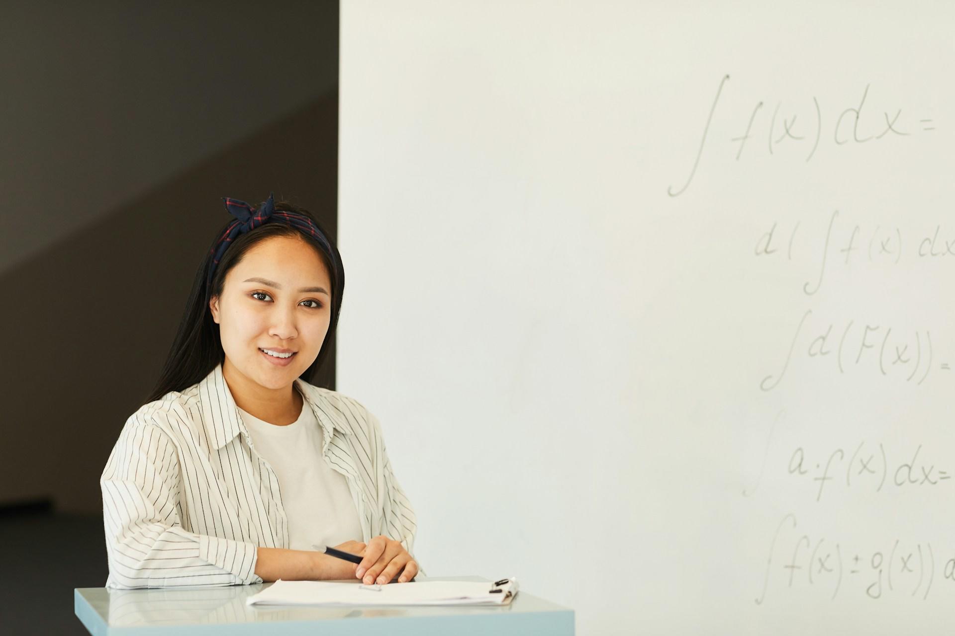 A woman sitting in front of a whiteboard, possibly explaining something.