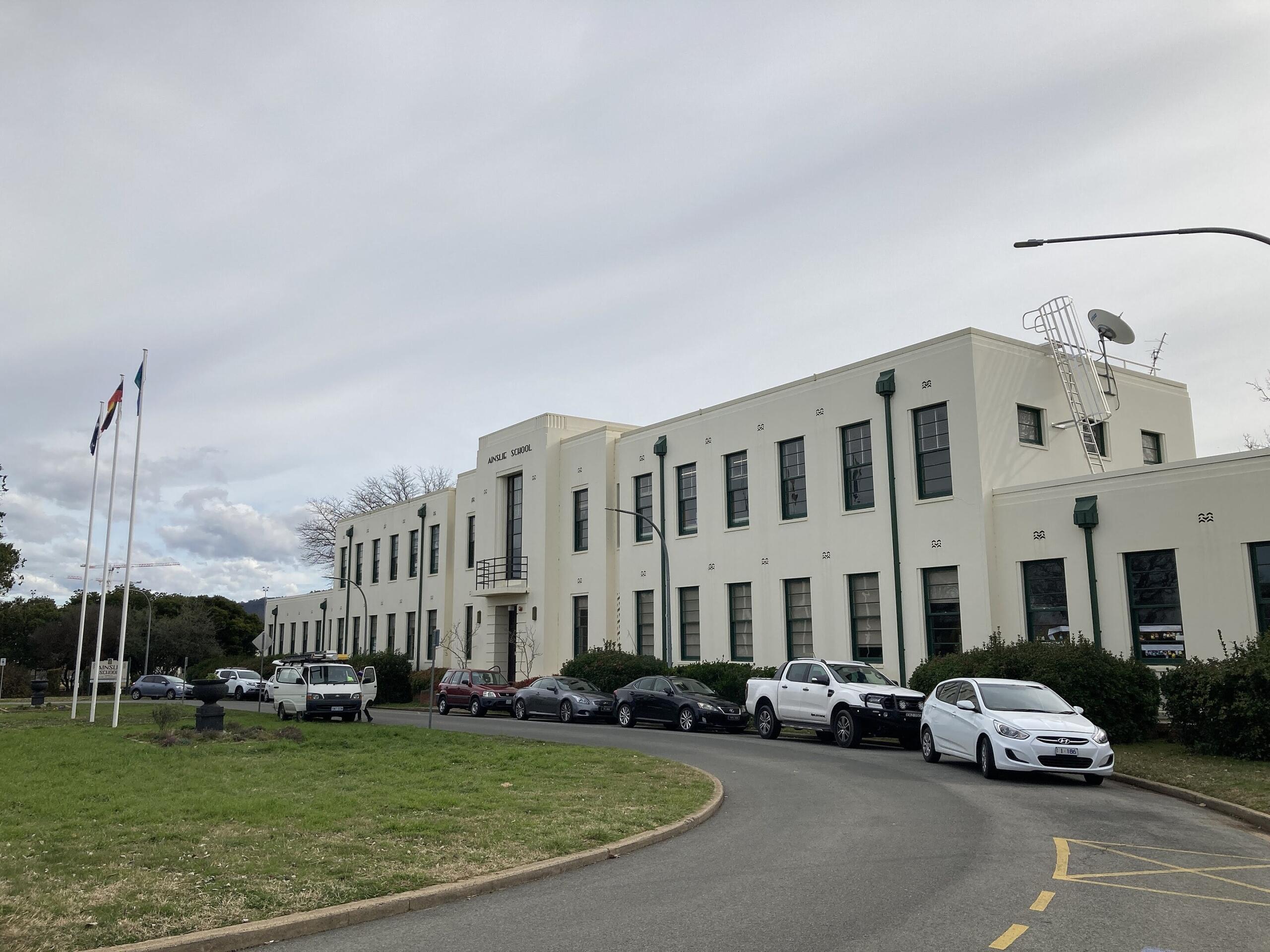 A large white building with cars in front on a cloudy day.