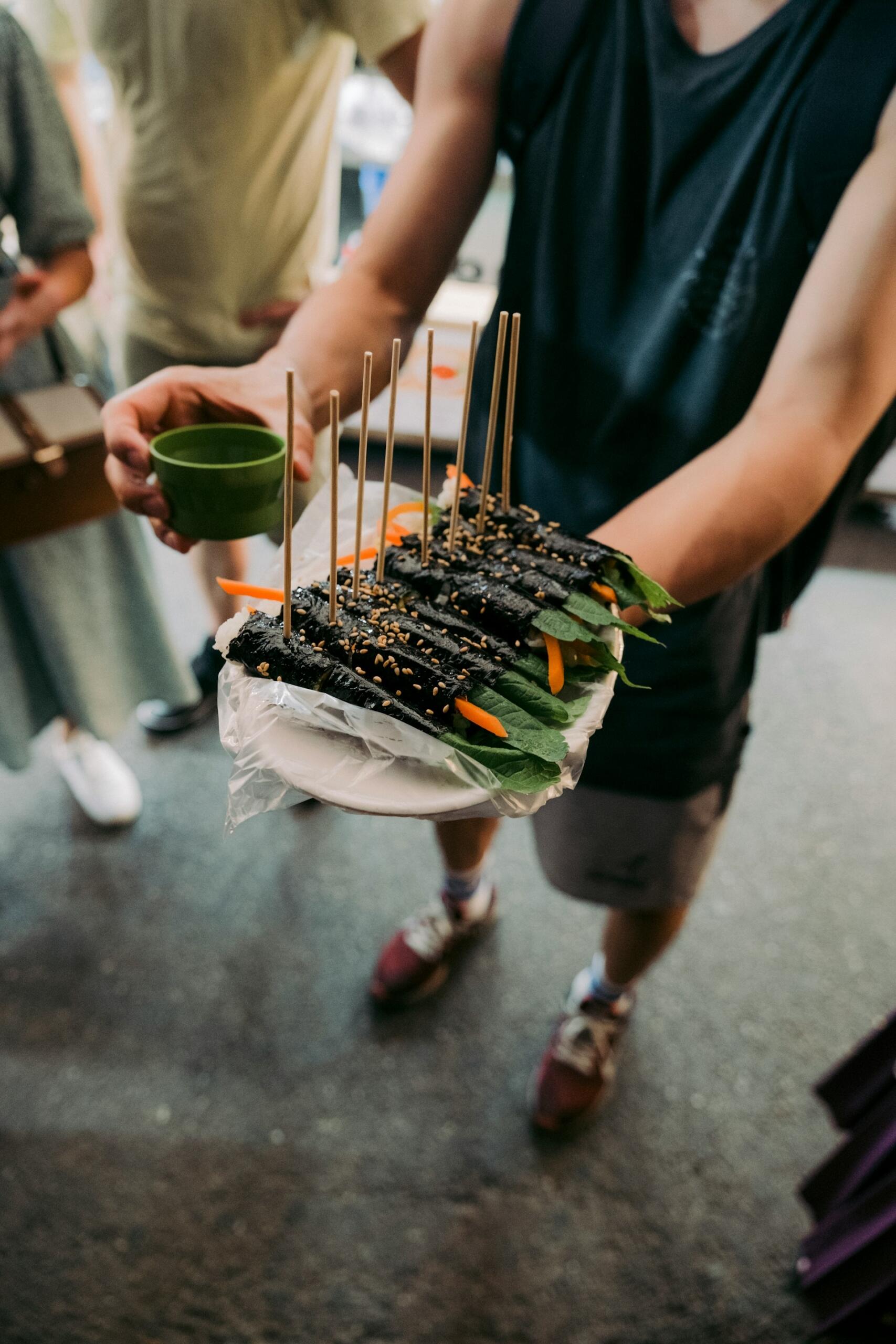 A person holding a plate of sushi and a small green cup.