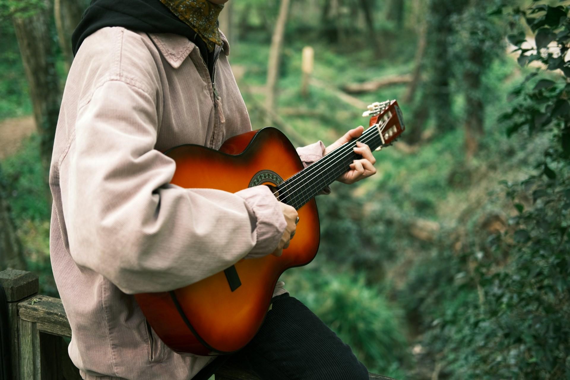 A person playing guitar in the woods.