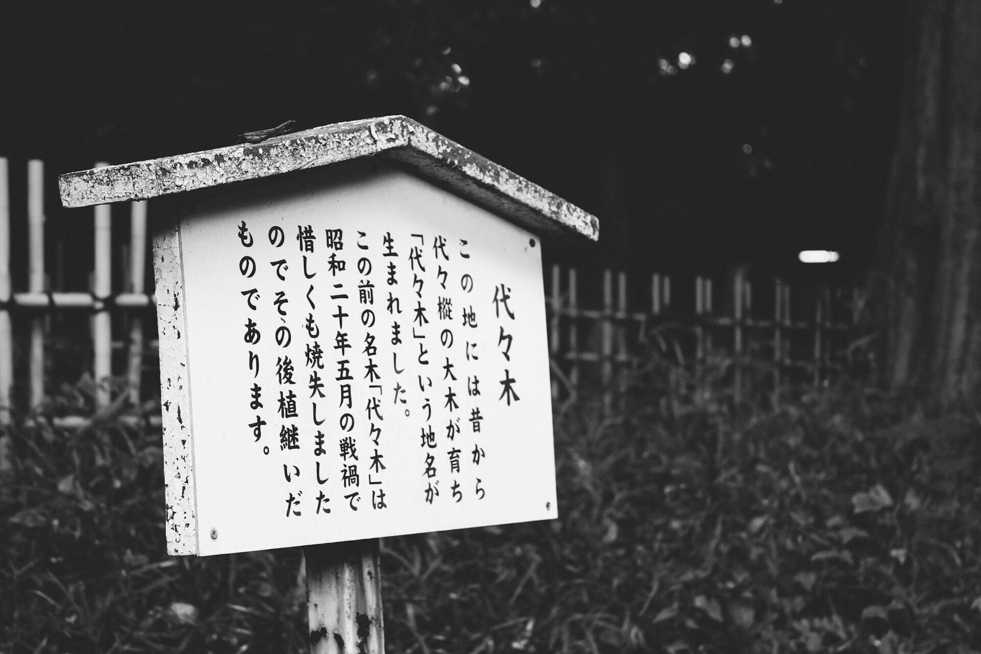 An outdoor sign featuring Japanese writing planted in a garden. 