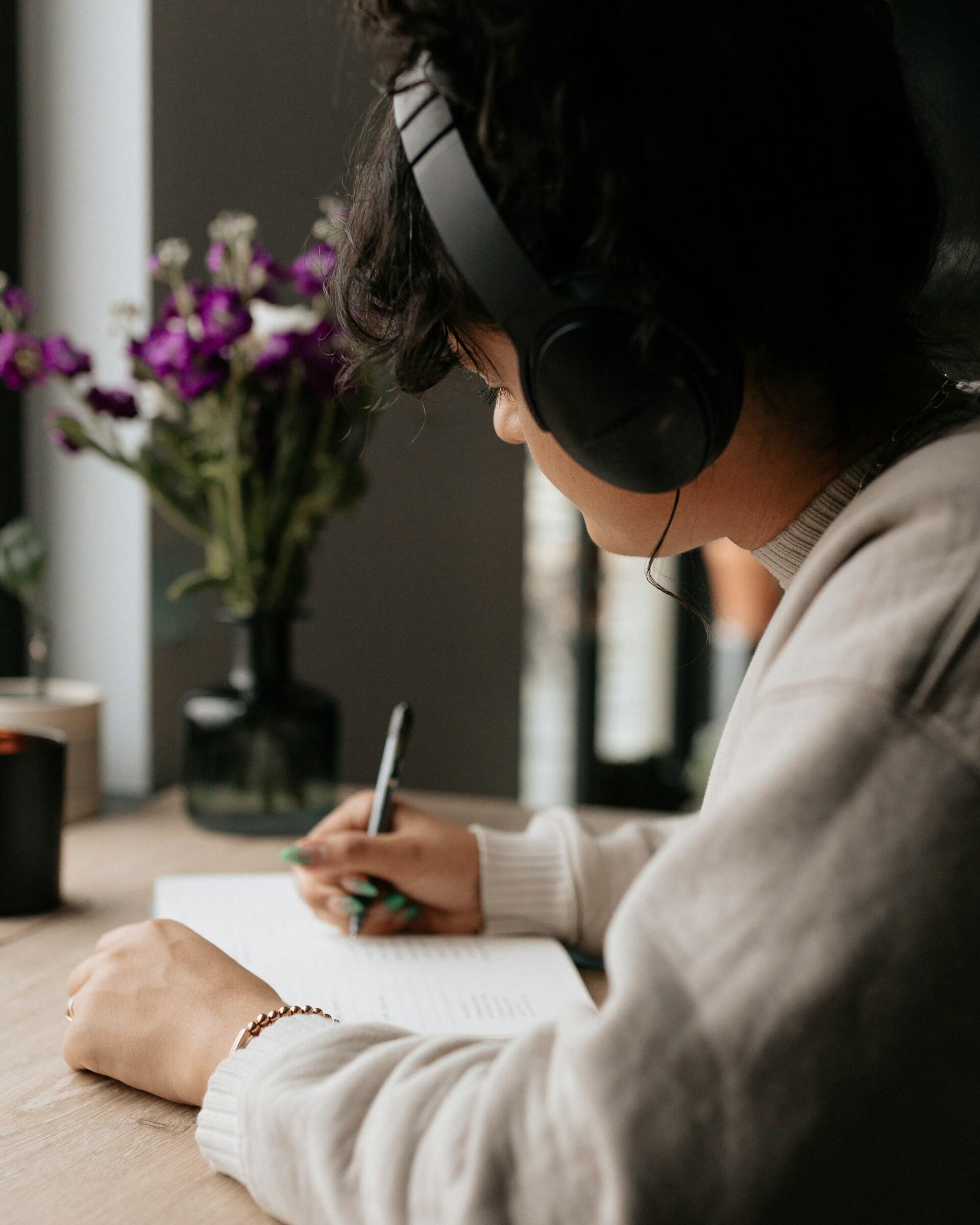 A person wearing headphones writes in a notebook.