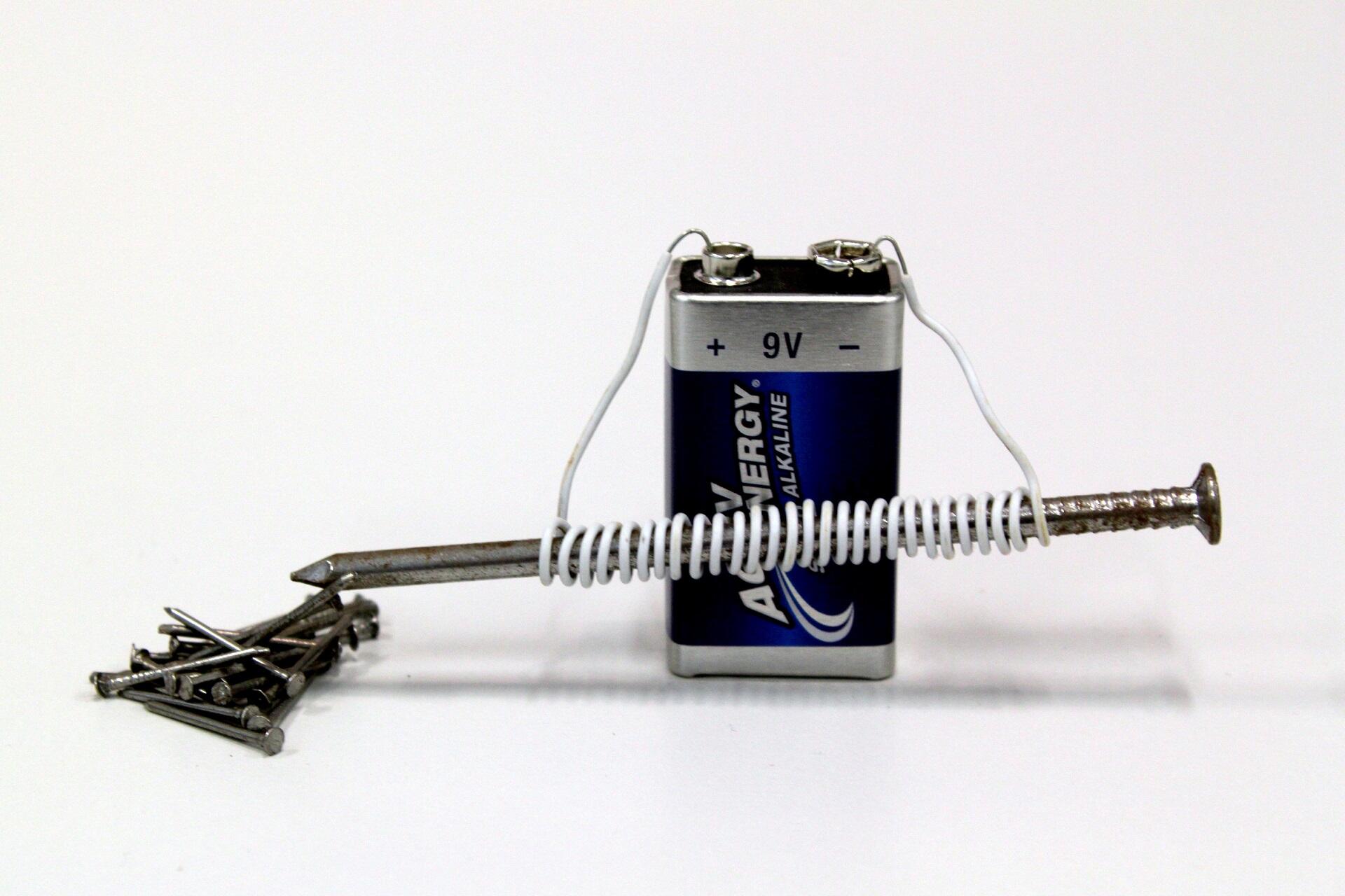 A 9-volt battery with a wire attached, wrapped around a nail, with metal at the nail's tips.