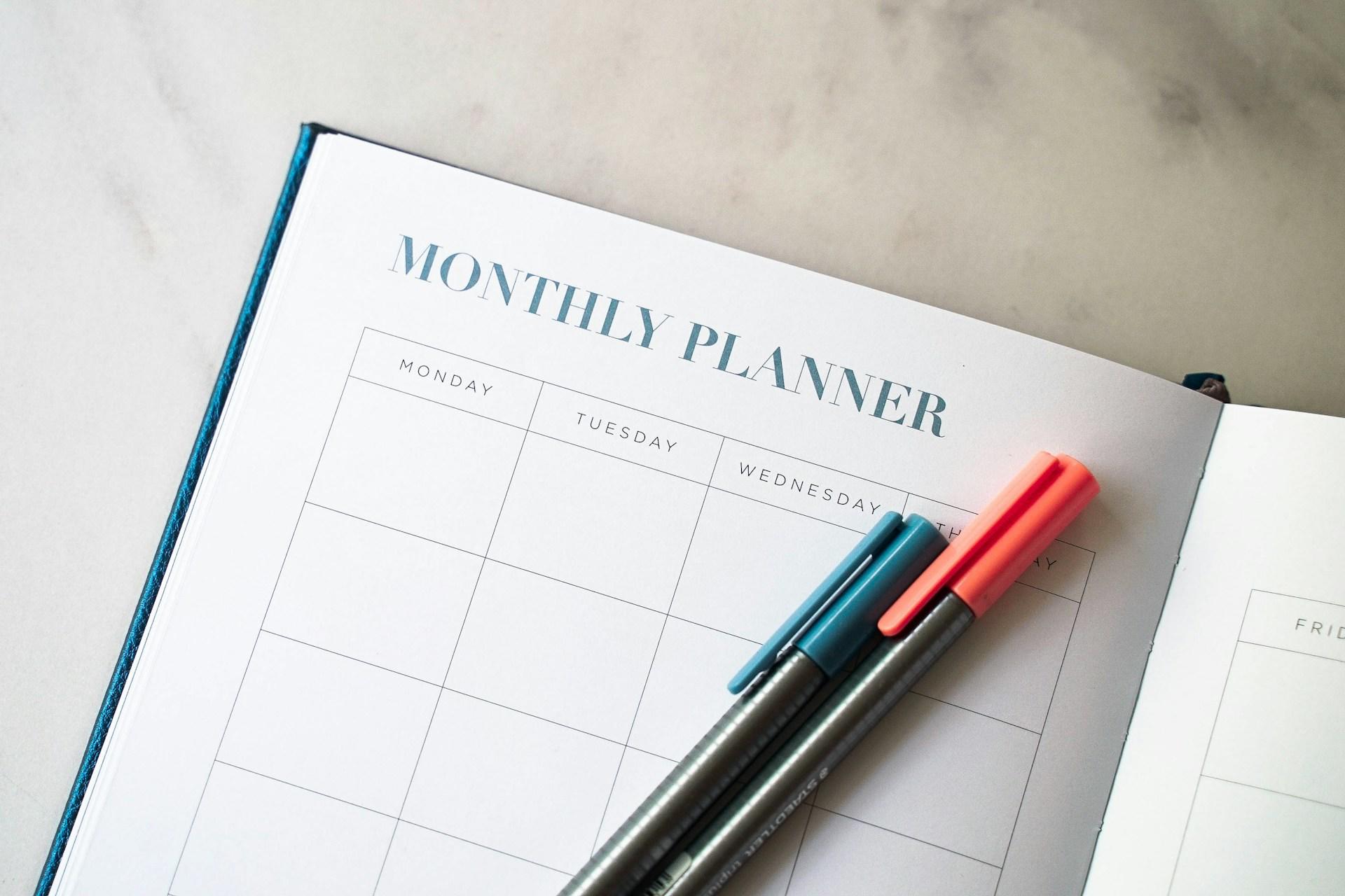 A monthly planner with two pens on it.