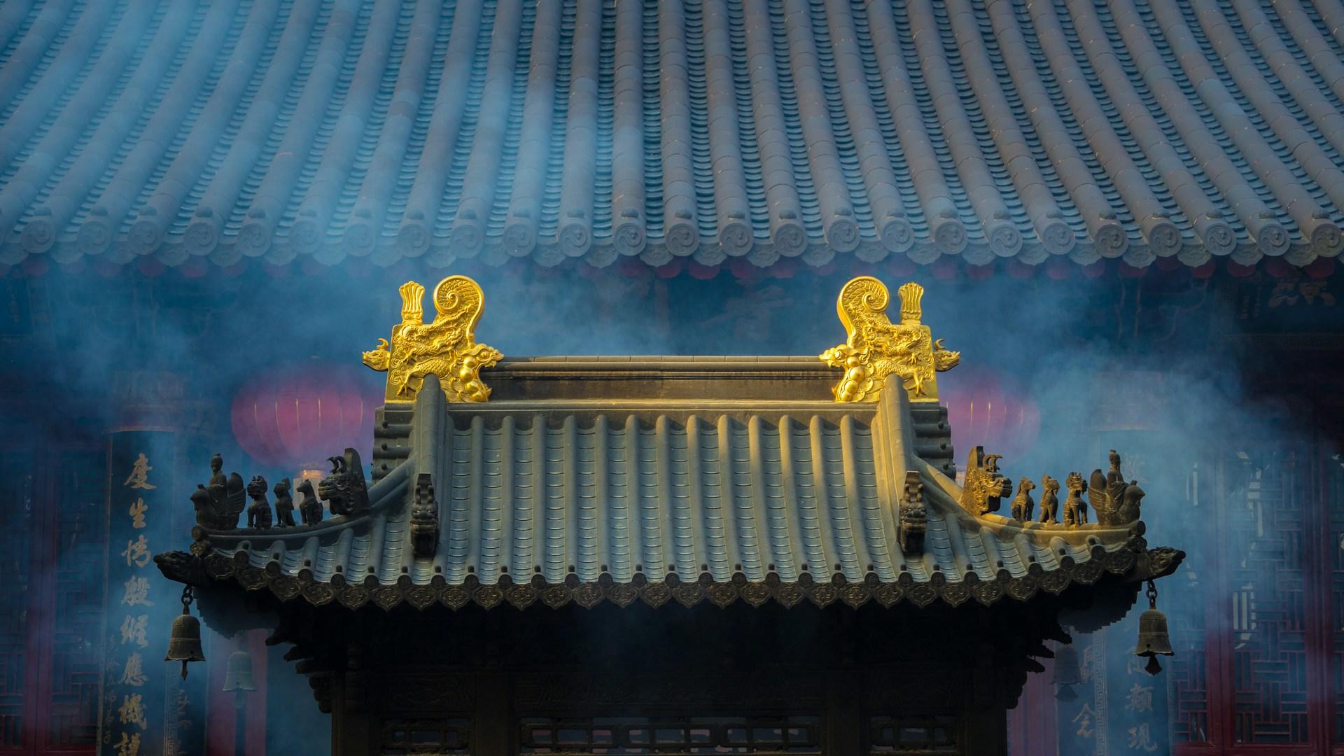 A traditional Chinese building with smoke billowing from its roof, set against a clear sky.