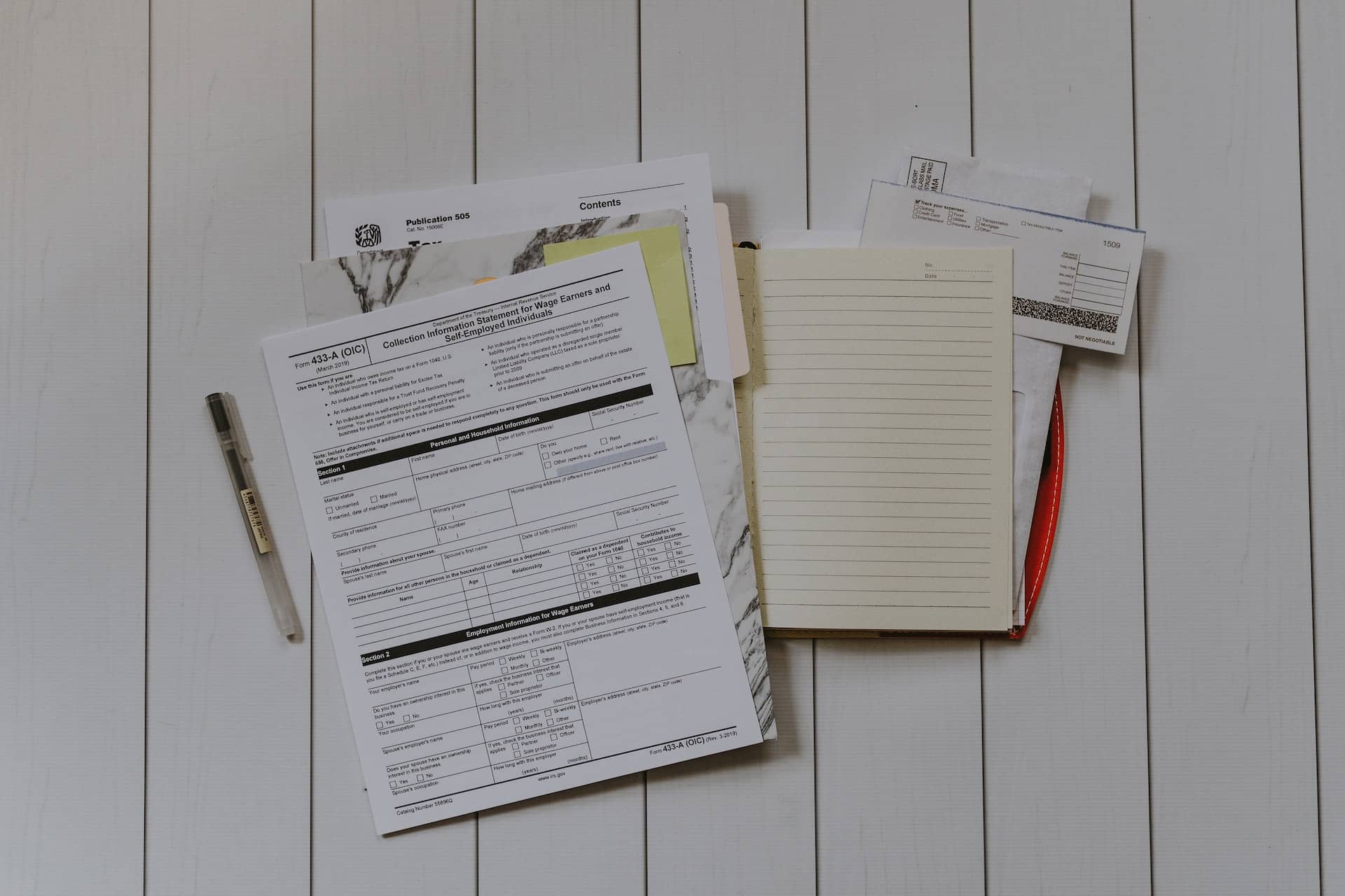 A stack of papers fanned over their open folder, resting on a pale coloured wooden slat table.