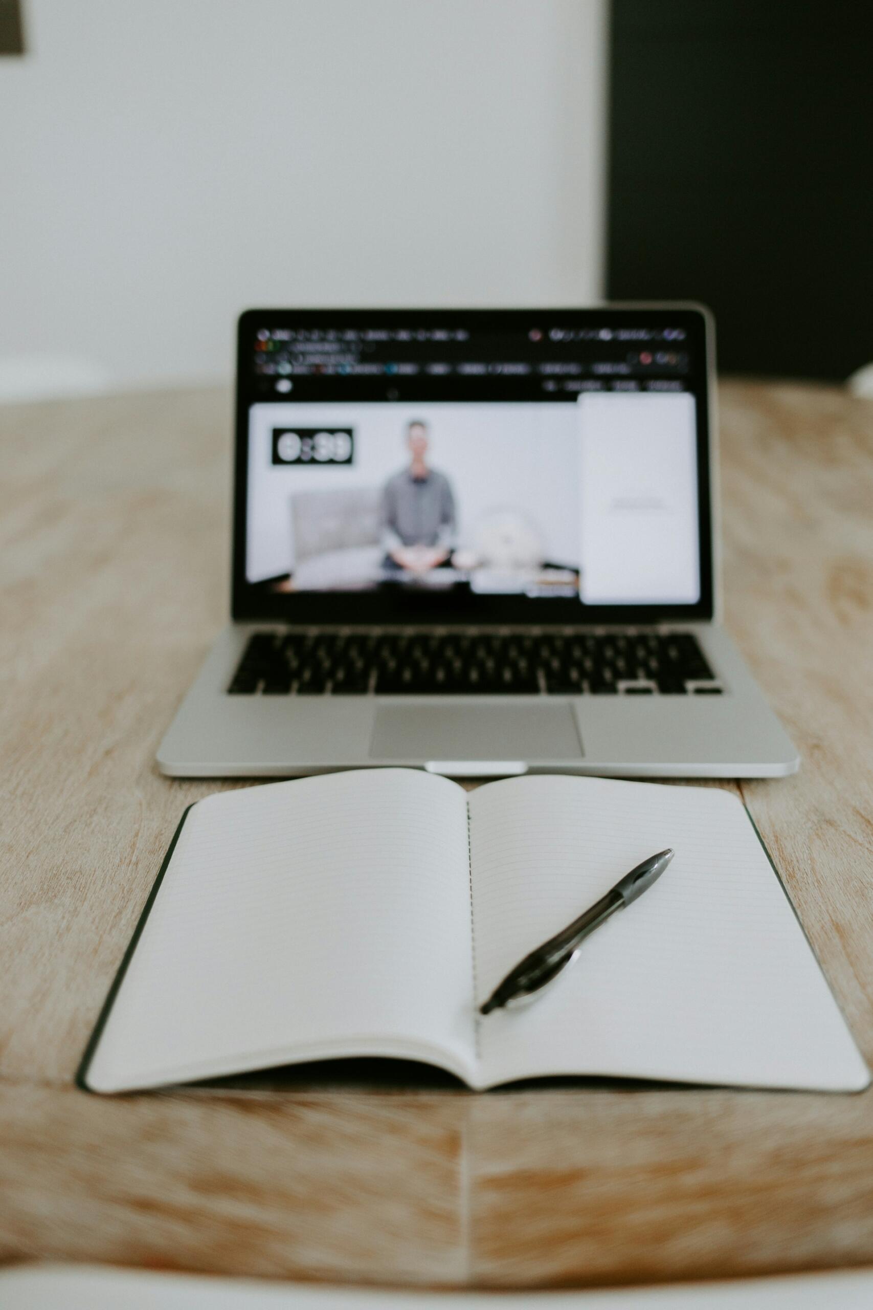 An open notebook and pen in front of a computer.