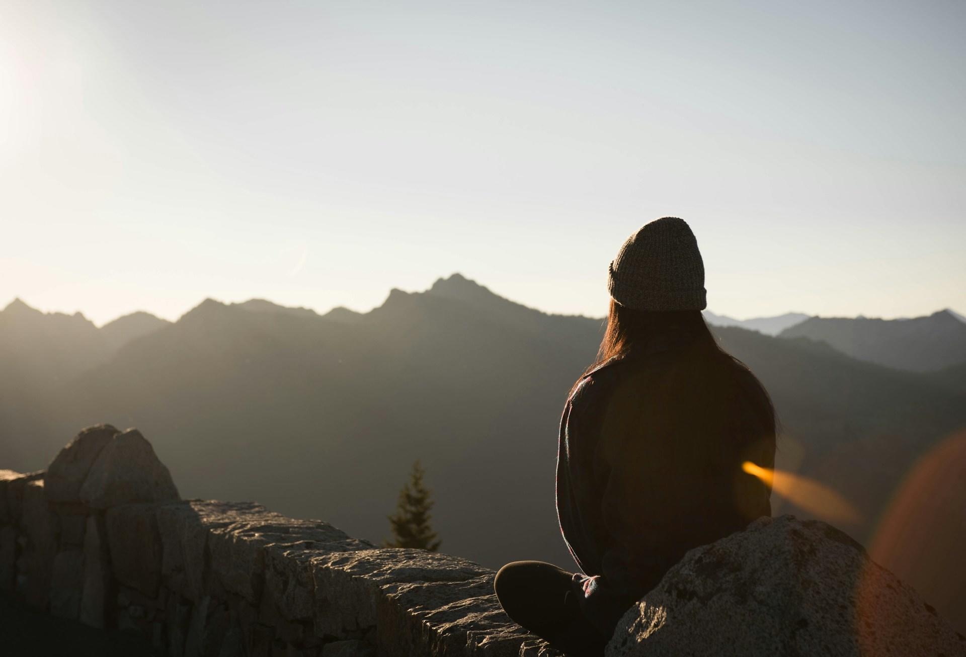 Woman enjoys scenic mountain vista from rocky perch.