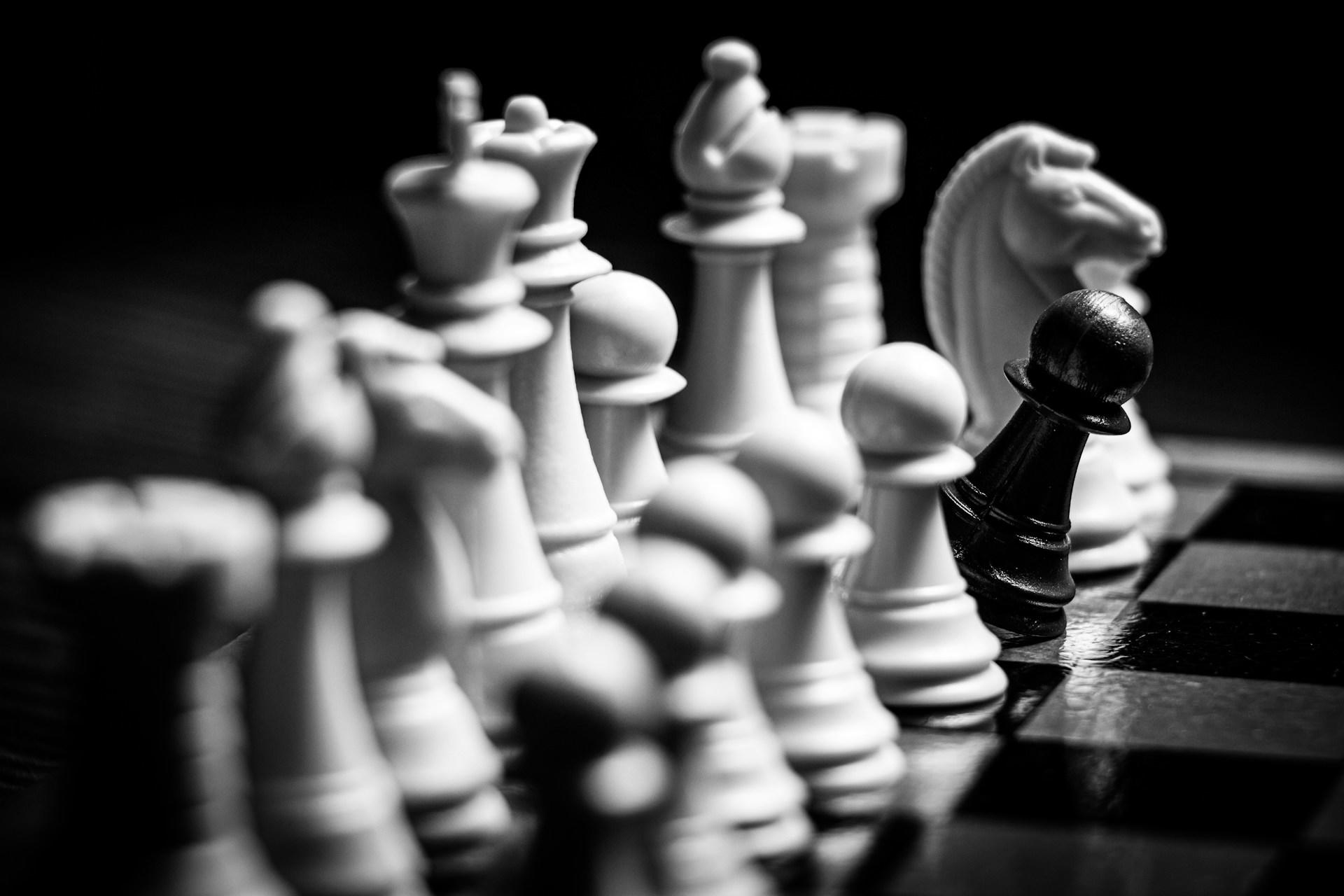 Black and white chess pieces on a board, focusing on a single black pawn.