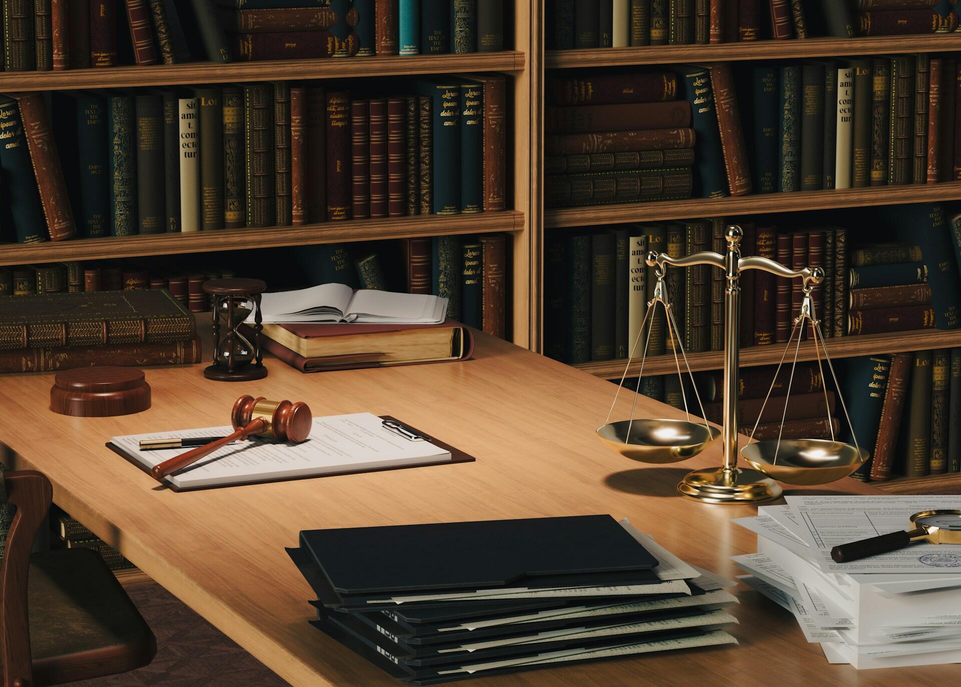A wooden desk with a gavel, scales of justice, books, and legal documents in a library setting.