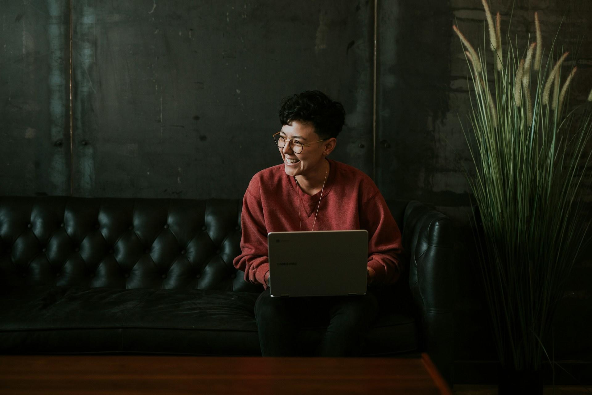 Woman sitting on couch with laptop, laughing.