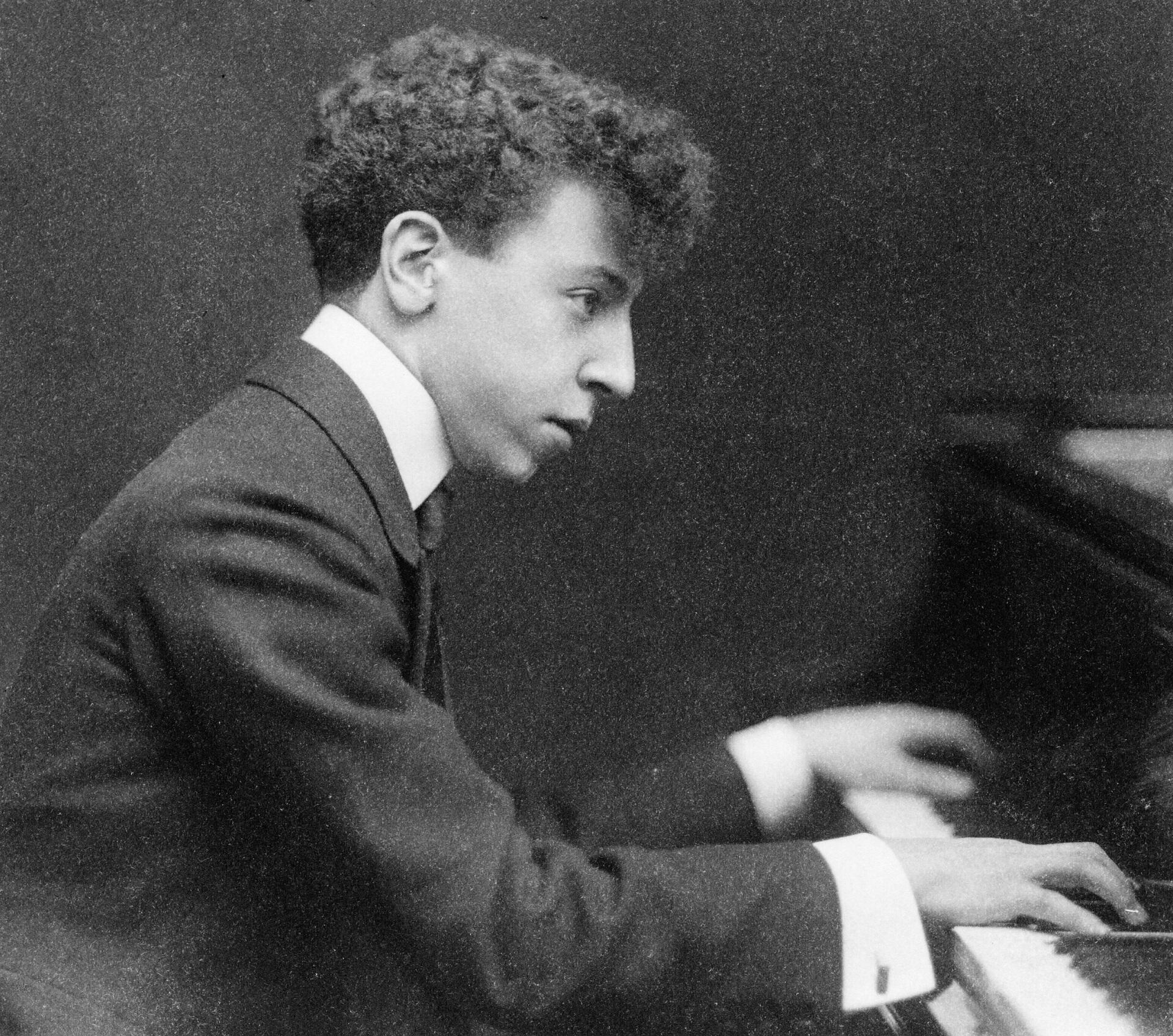 Arthur Rubinstein, half-length portrait, seated at piano, facing right.